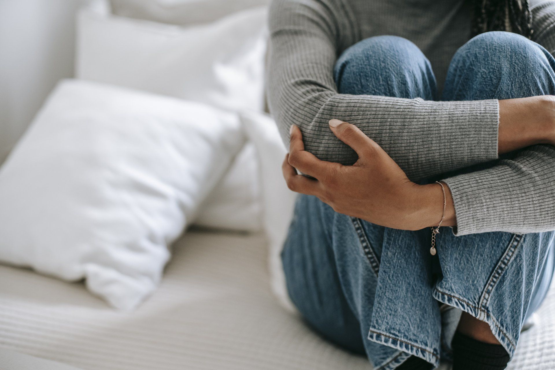 Woman sitting on her bed hugging her knees in discomfort