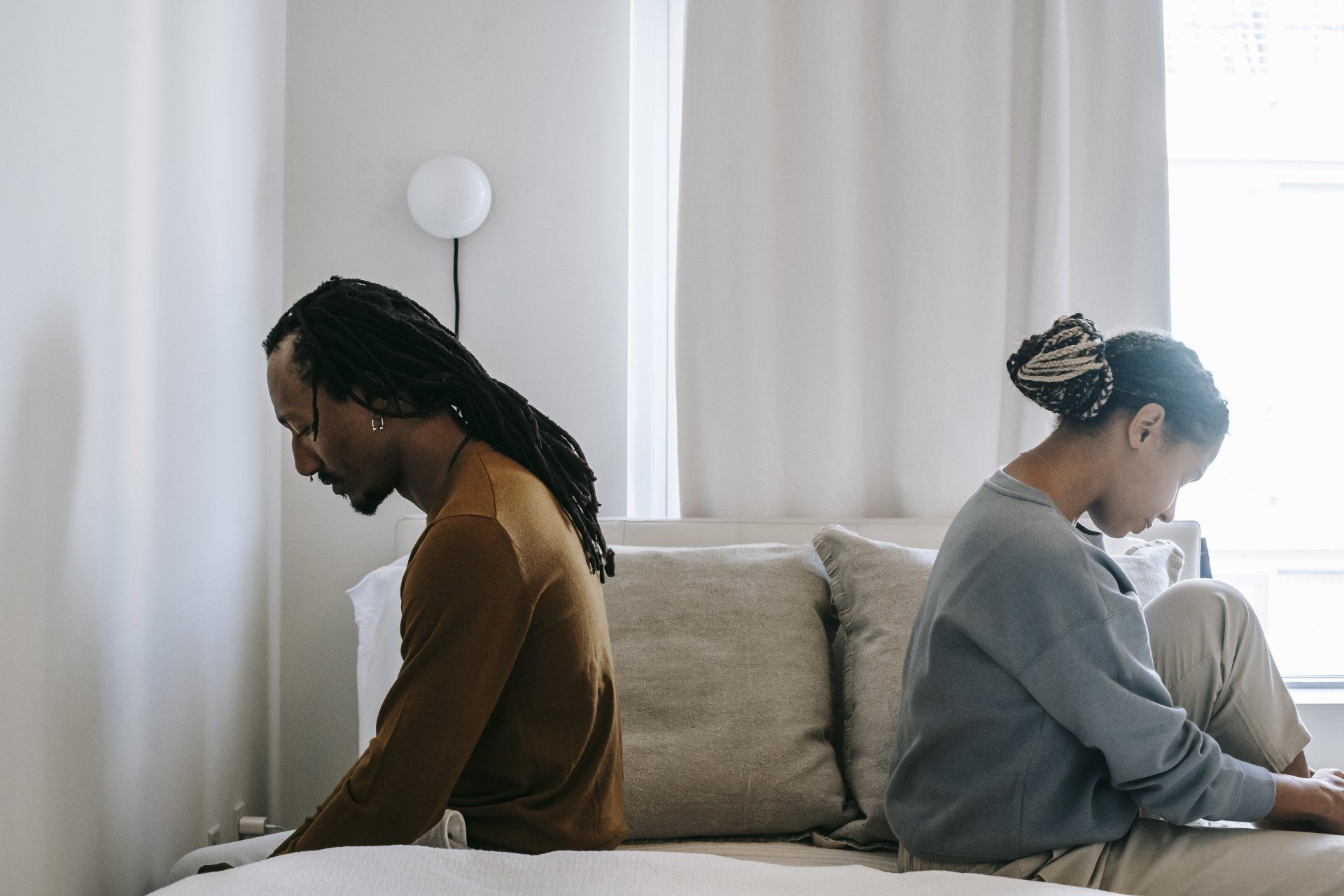A man and a woman are sitting back to back on a couch.