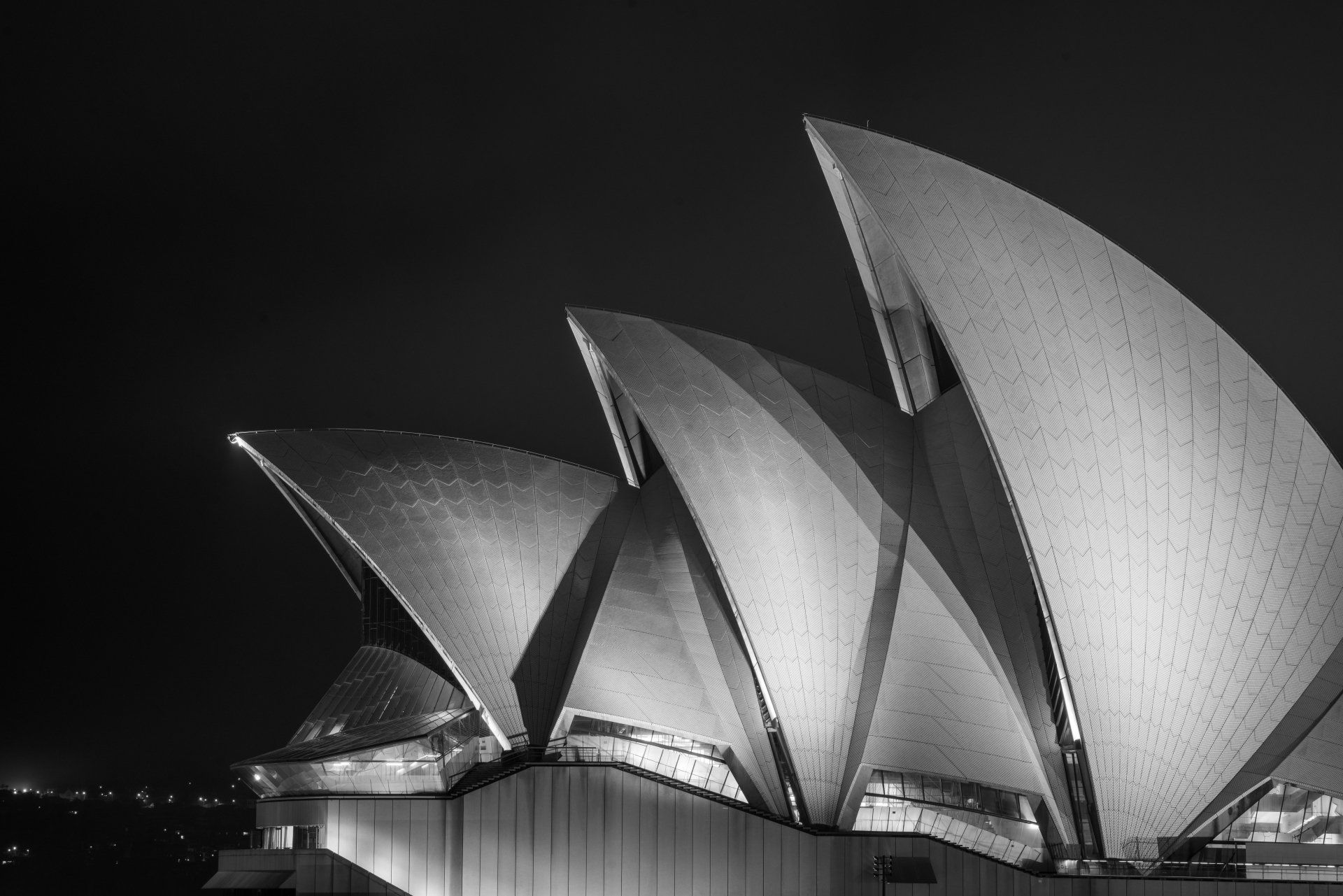 A Ópera de Sydney à noite, iluminada de branco contra um céu escuro.