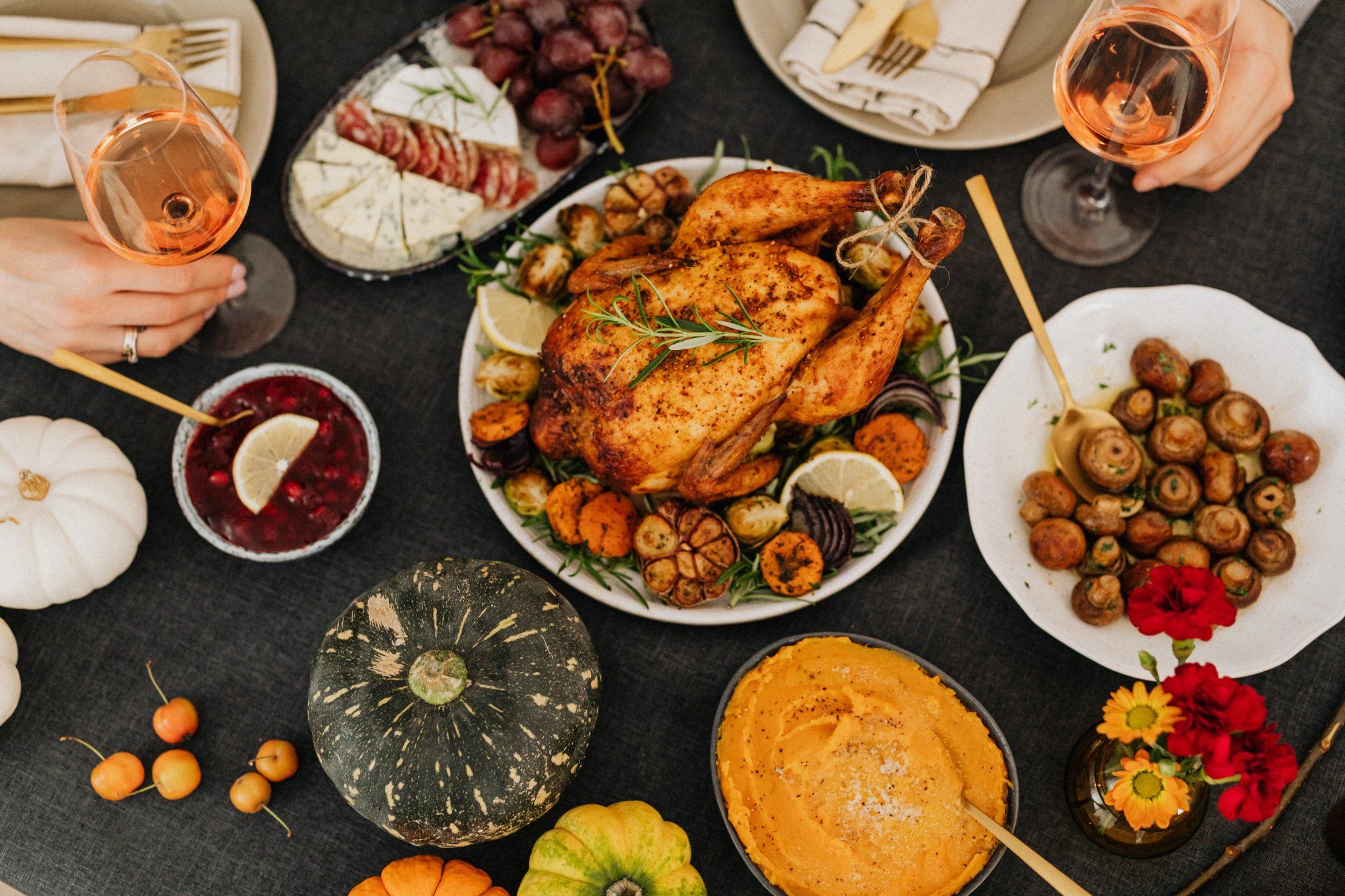 Thanksgiving table spread with roasted turkey, pumpkins, side dishes, wine glasses.