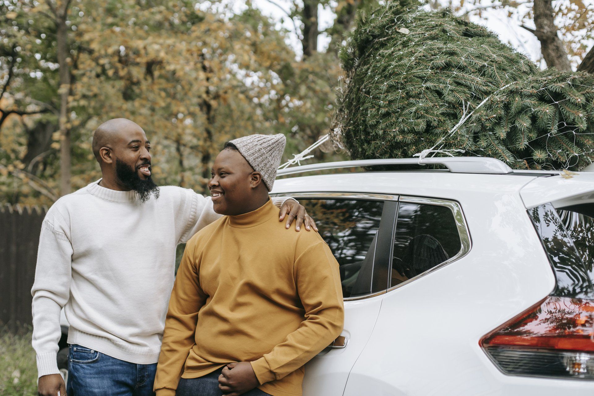 Two men are standing next to a car with a christmas tree in the back.