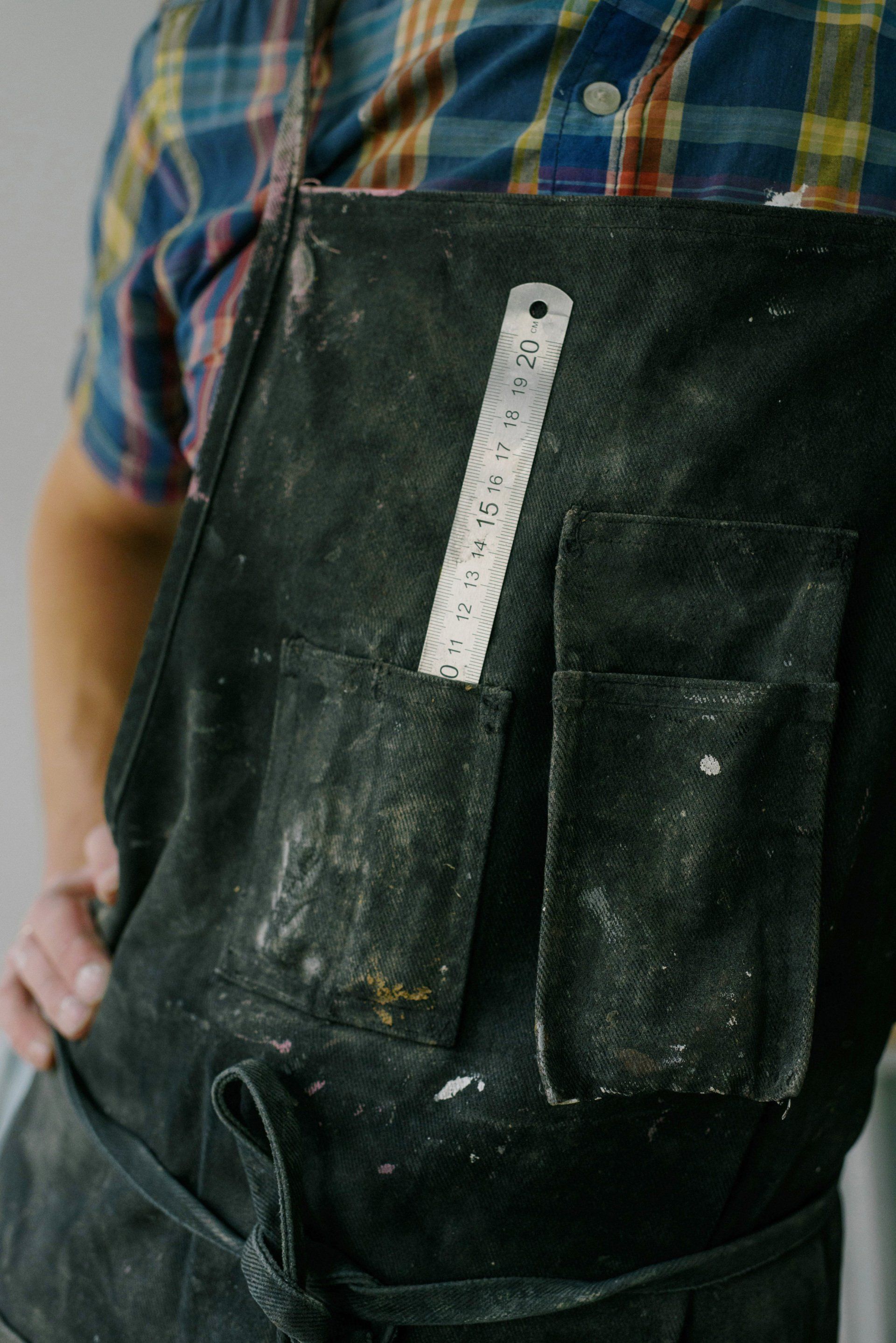 Person wearing a black apron with paint stains and a white ruler in the chest pocket