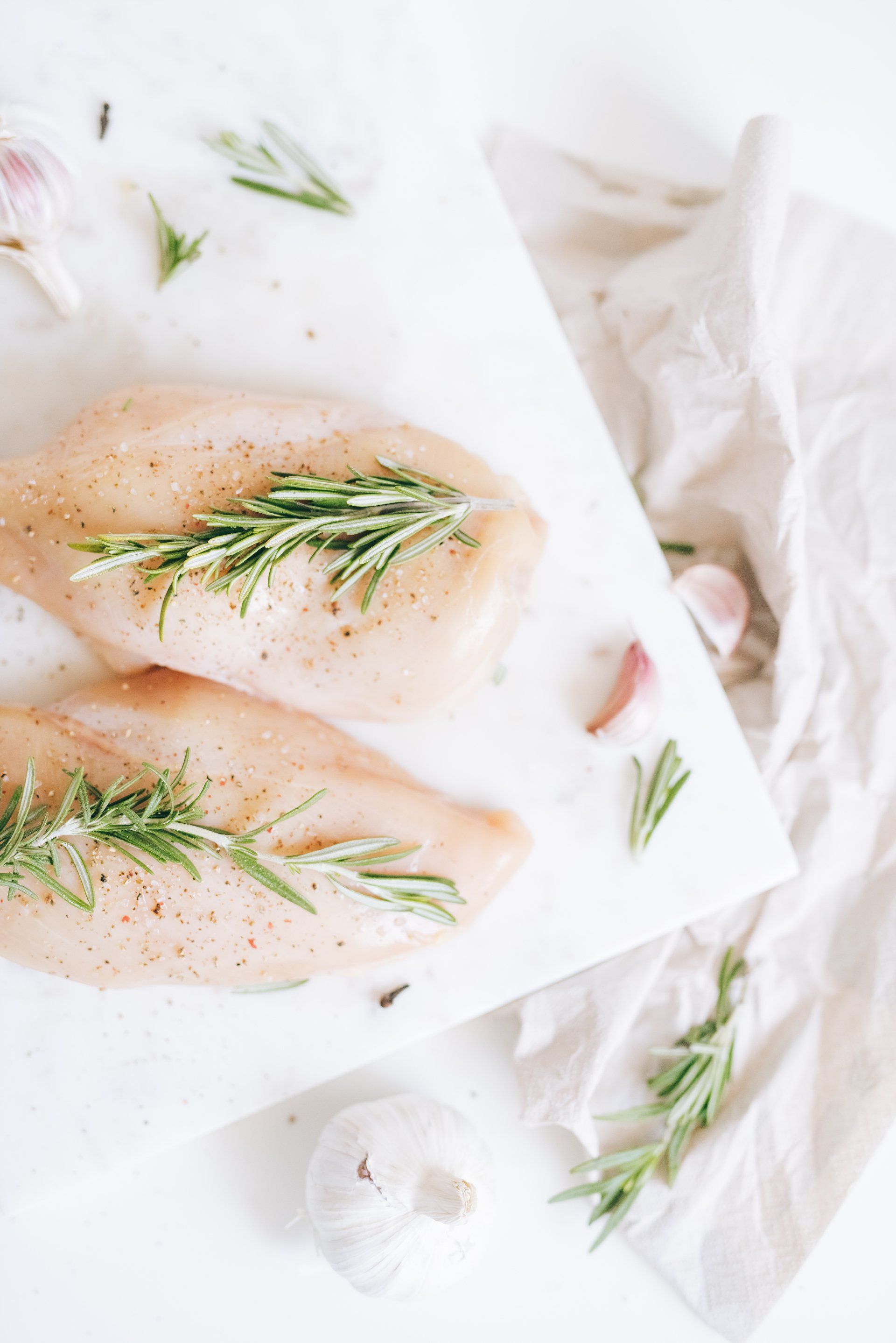 Raw chicken breasts seasoned with rosemary and garlic on parchment paper