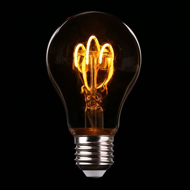 A vintage-style light bulb against a black background with glowing golden filaments creating warm, elegant curves of light, symbolizing how knowledge illuminates the path forward in patient-led public policy initiatives for autoinflammatory arthritis advocacy.