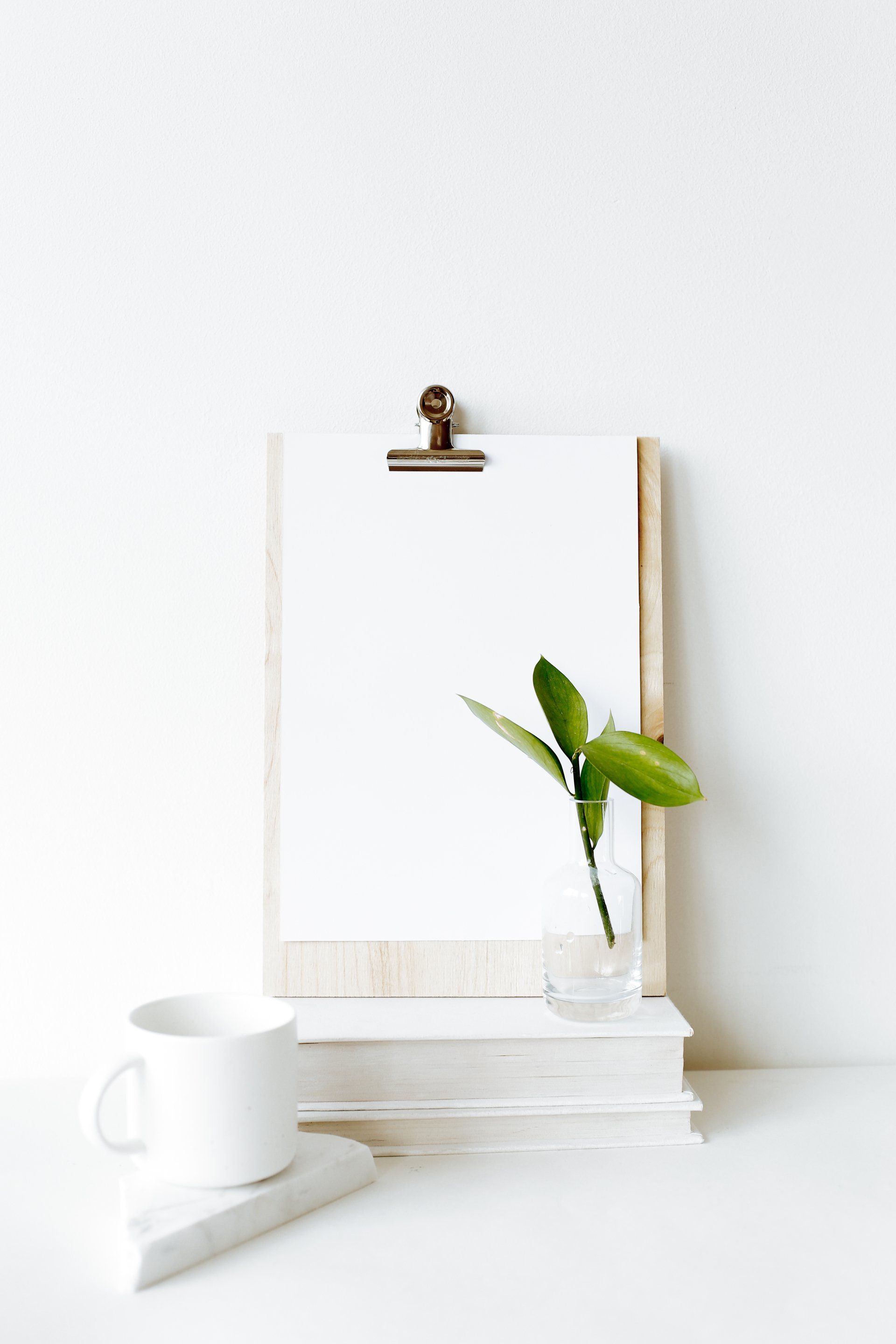 A clipboard with a plant in a vase on top of a stack of books.