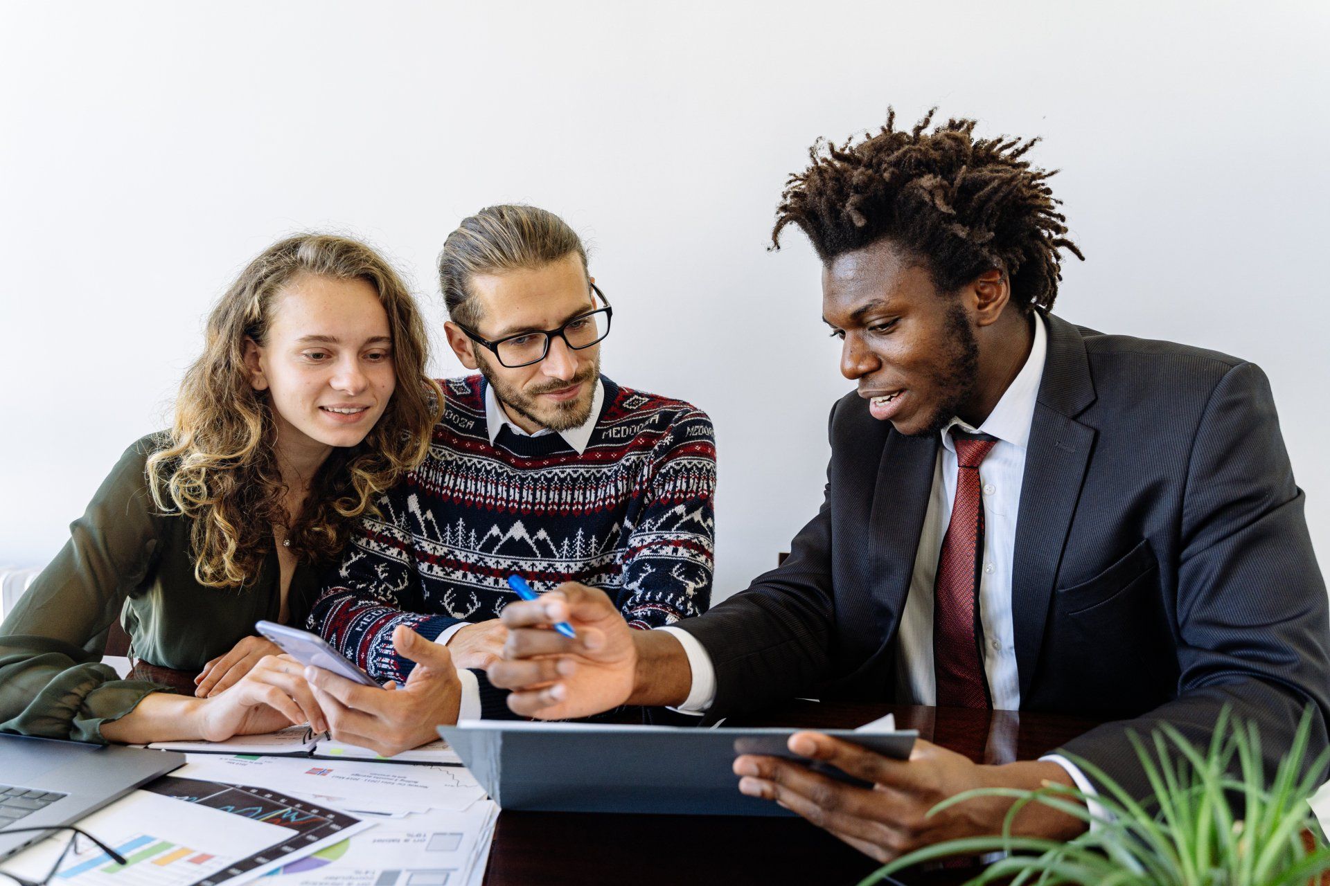 A group of people are sitting at a table looking at a tablet.