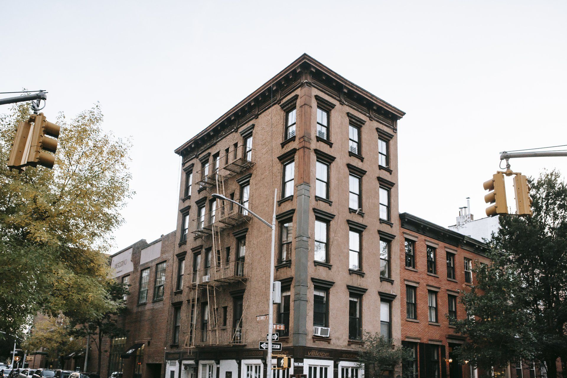 Brick building on a city corner, with fire escape, traffic lights, and trees in the background.