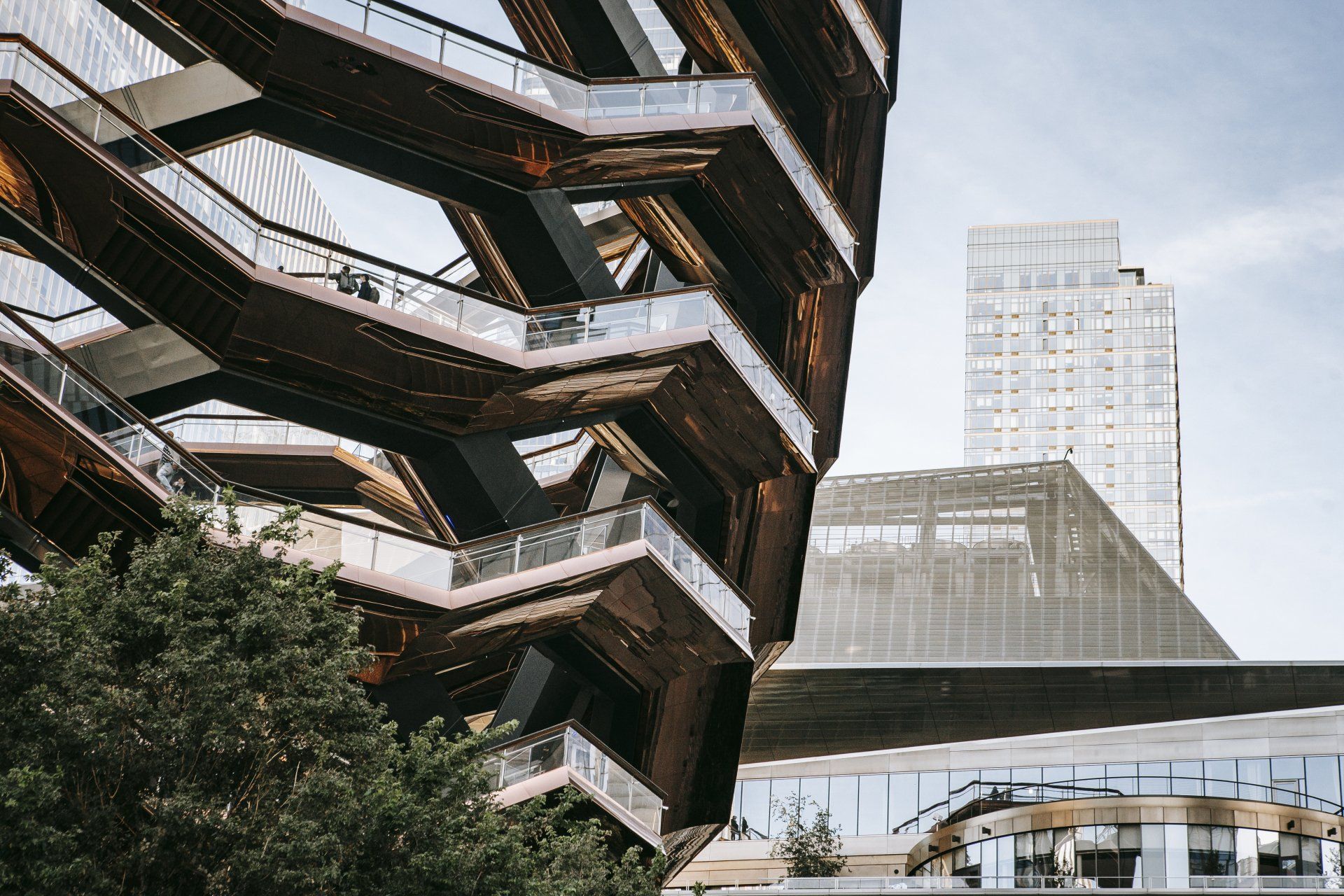 Modern angular building beside a glass skybridge and high-rise tower in an urban setting