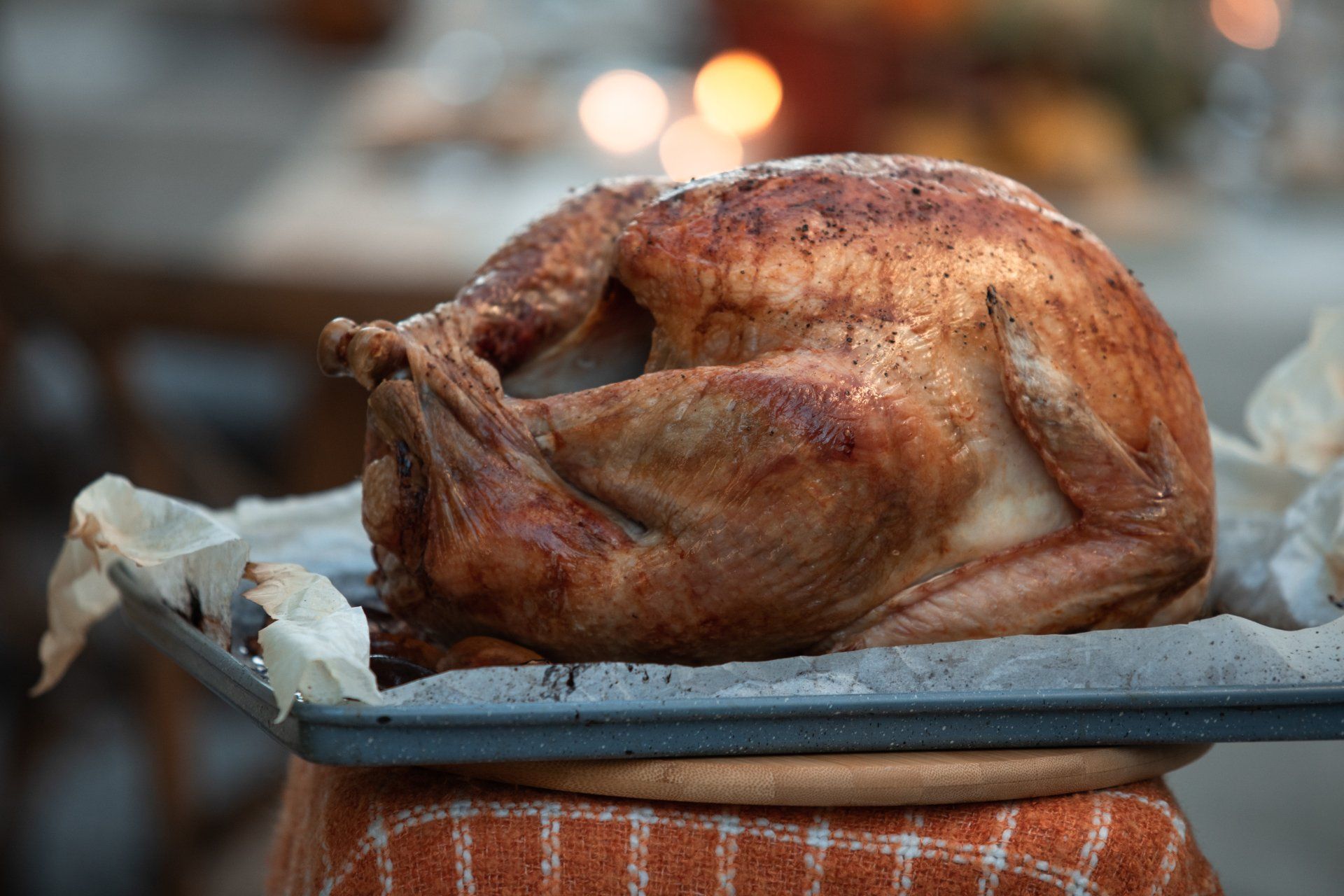 A roasted turkey on a baking sheet lined with parchment paper, resting on a wooden board covered with a plaid cloth.