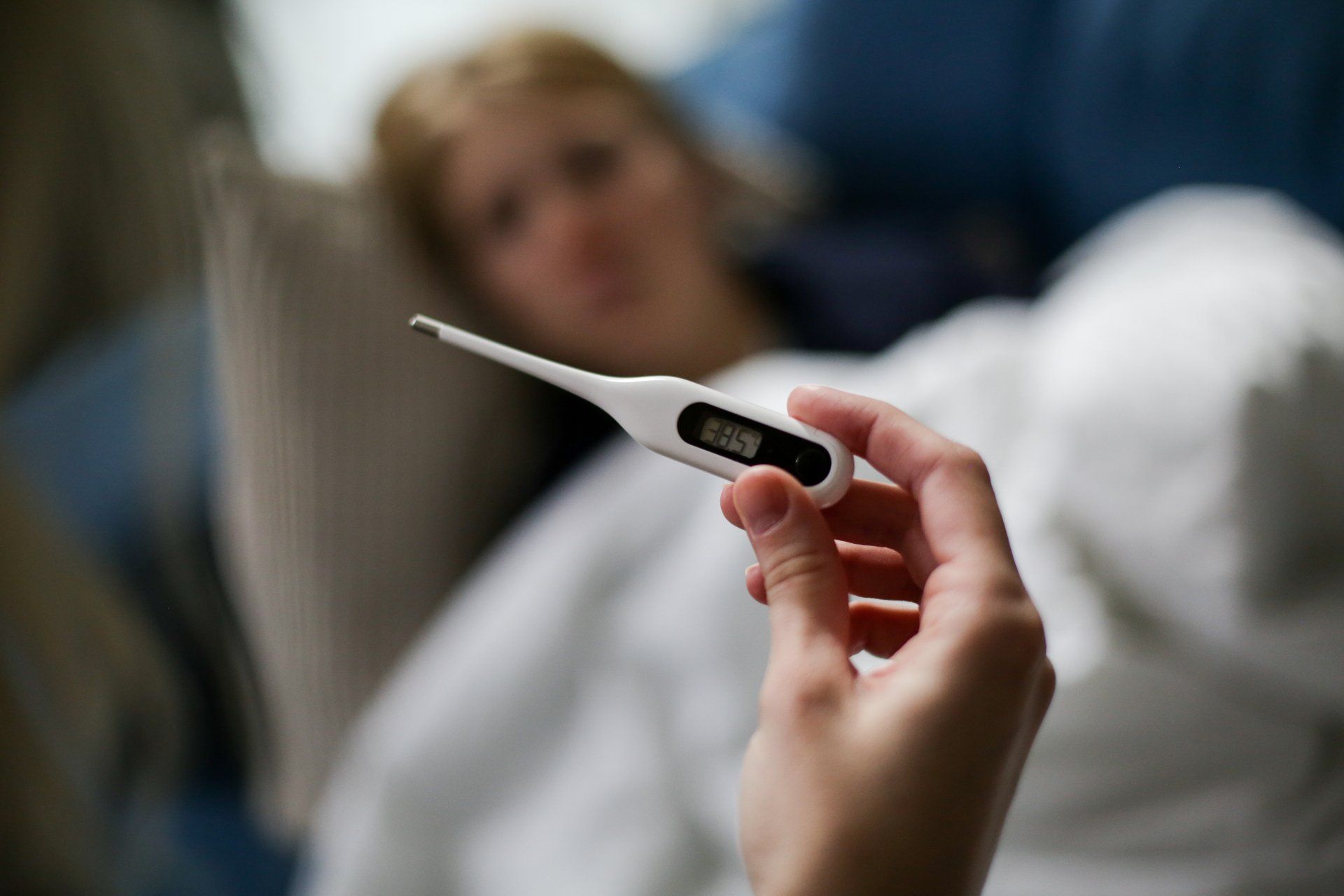 A person is holding a thermometer in front of a child laying in bed.