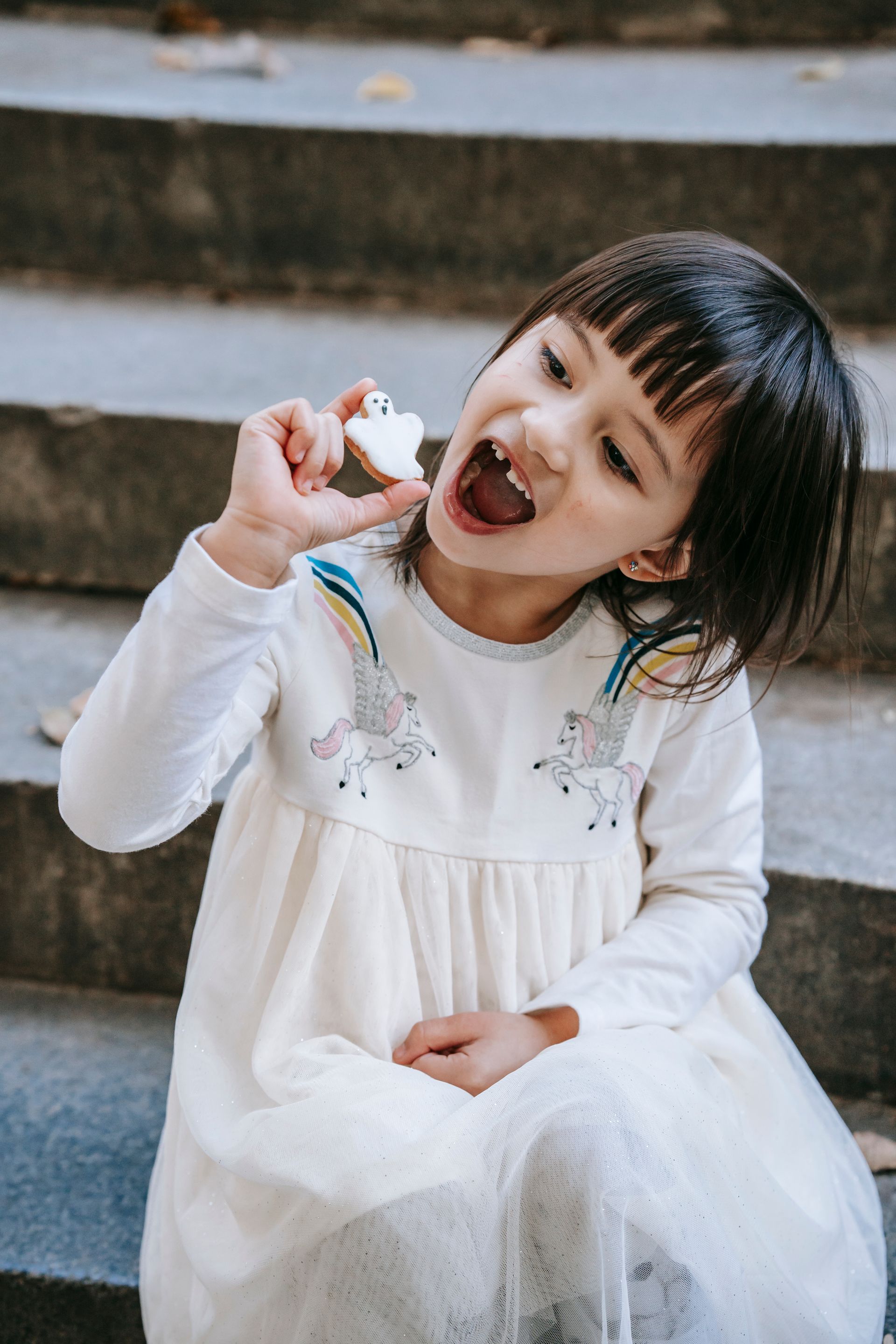 Girl eating a cookie, seated on concrete steps, wearing a white dress.