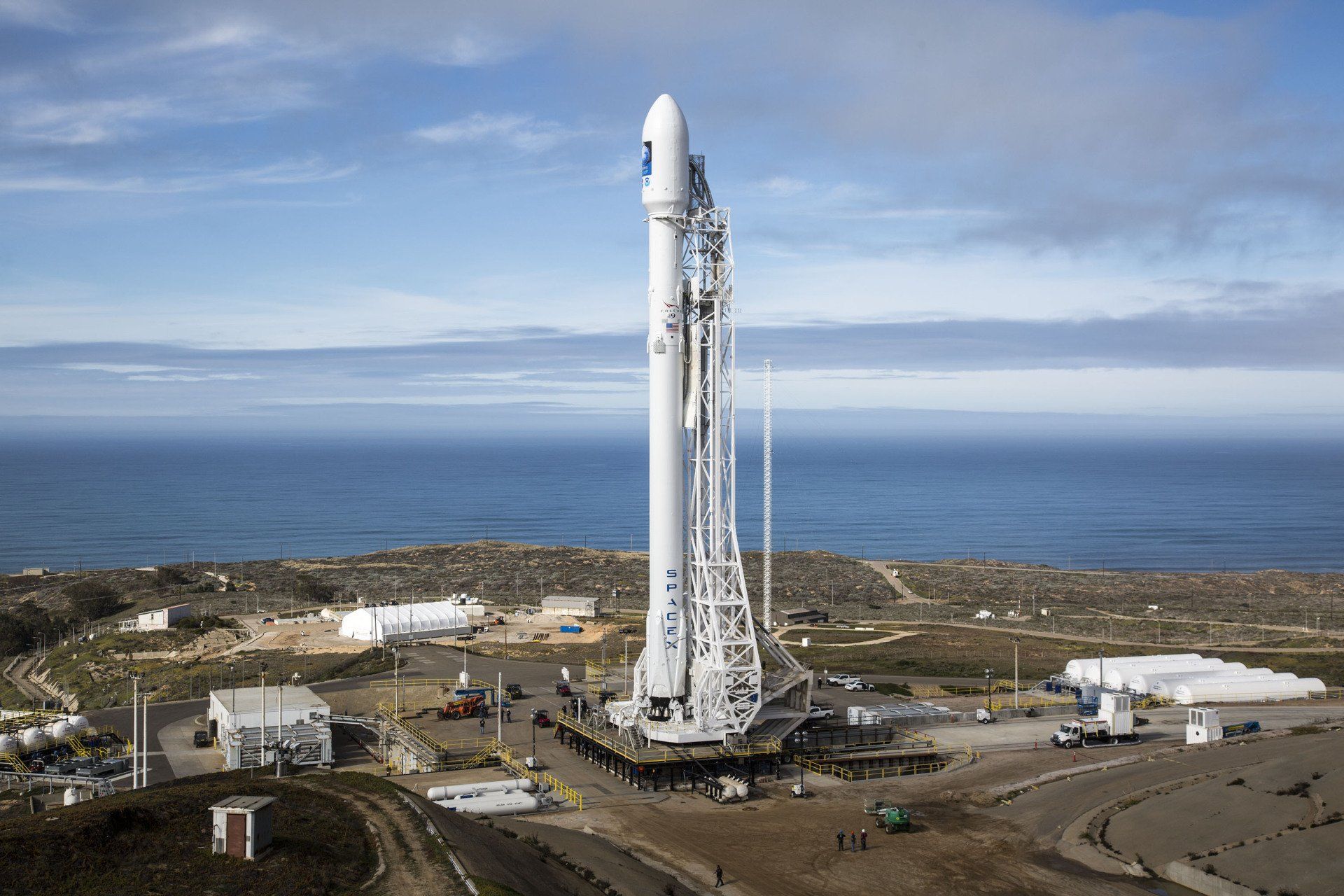 An aerial view of a rocket on a launch pad near the ocean.