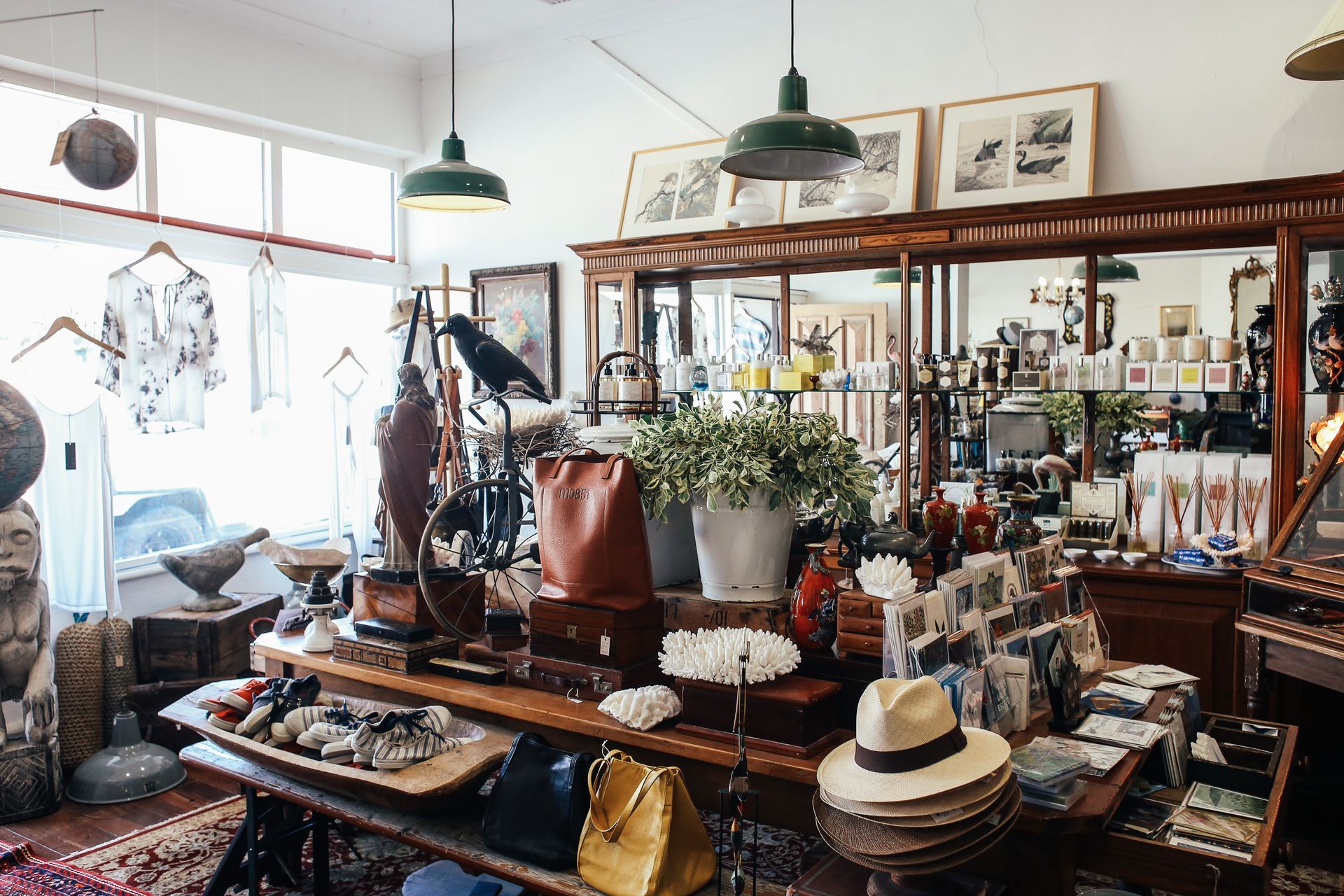 Boutique interior filled with antiques, art, and clothing displayed on tables and shelves, natural light.