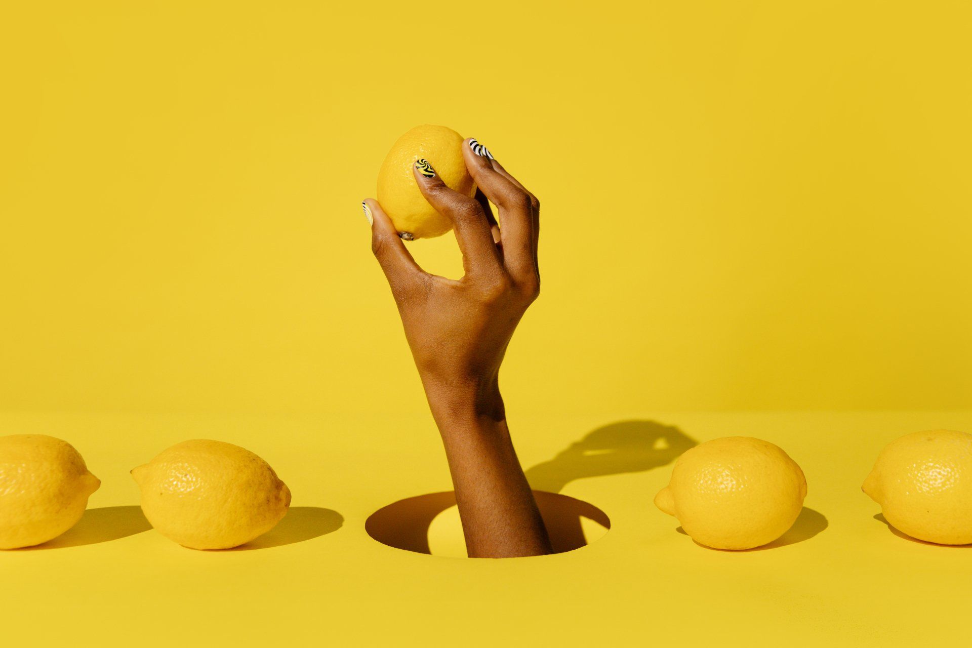 Hand emerging from a hole among yellow lemons on a yellow background