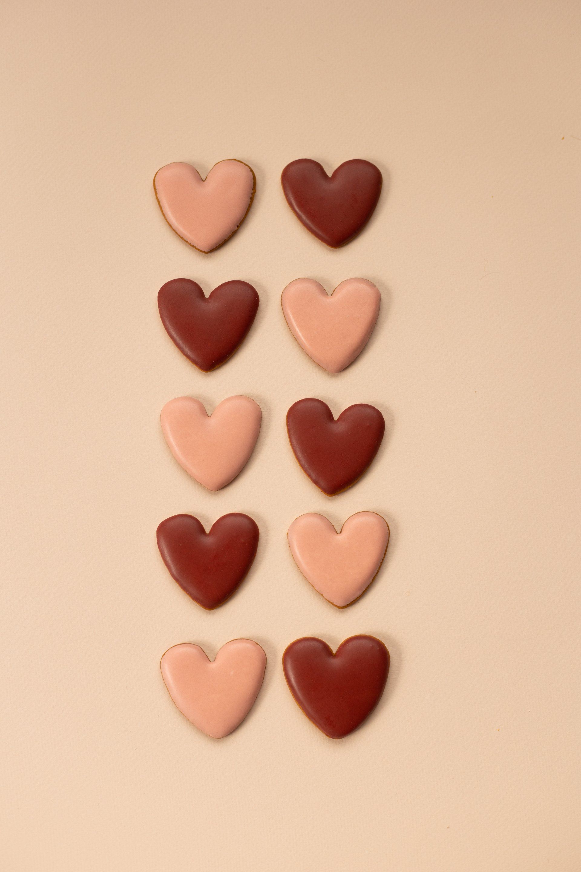 Ten heart-shaped cookies arranged in two vertical columns, alternating between light pink and deep reddish-brown colors.