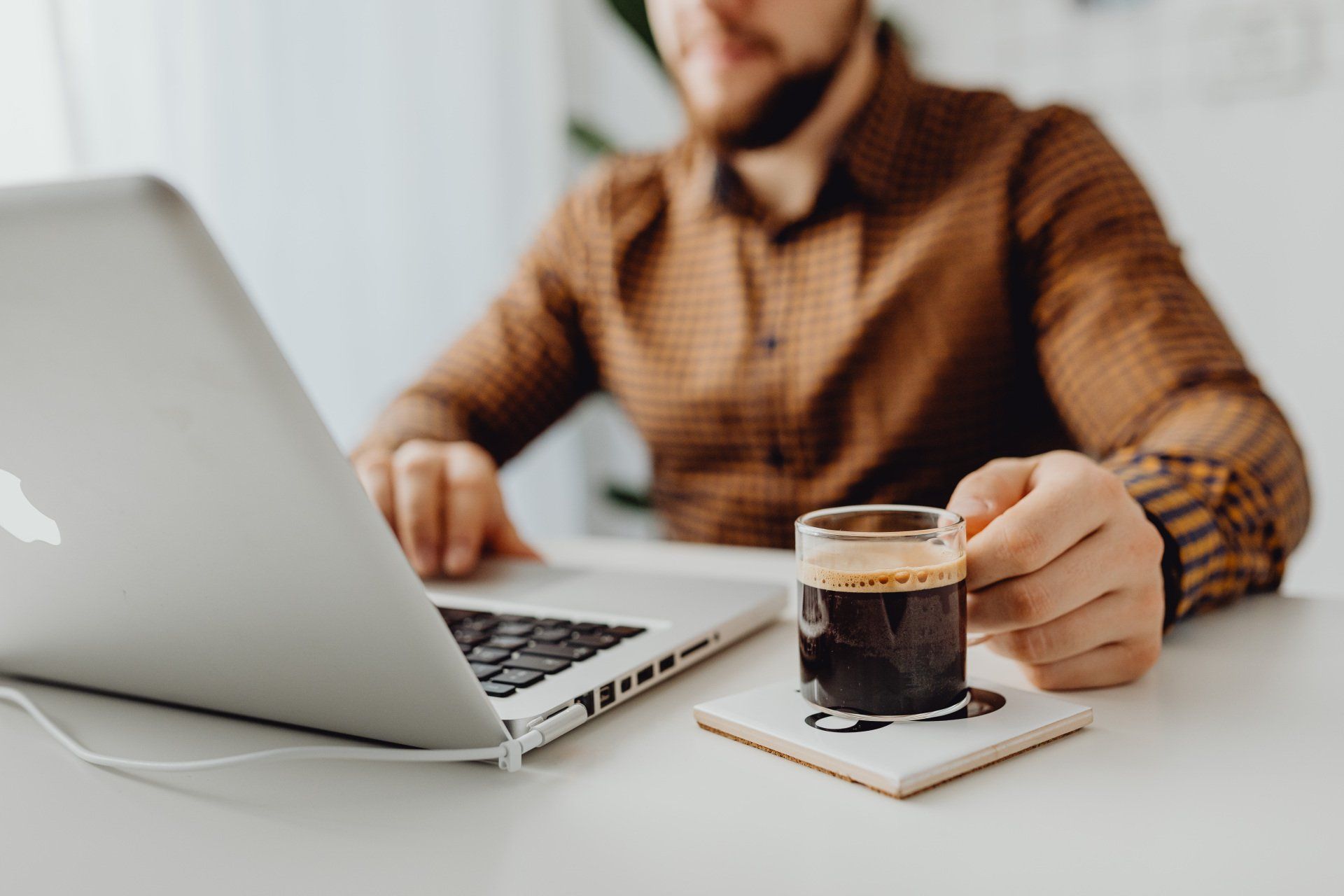A Virtual Assistant is sitting at a desk using a laptop computer while holding a cup of coffee.