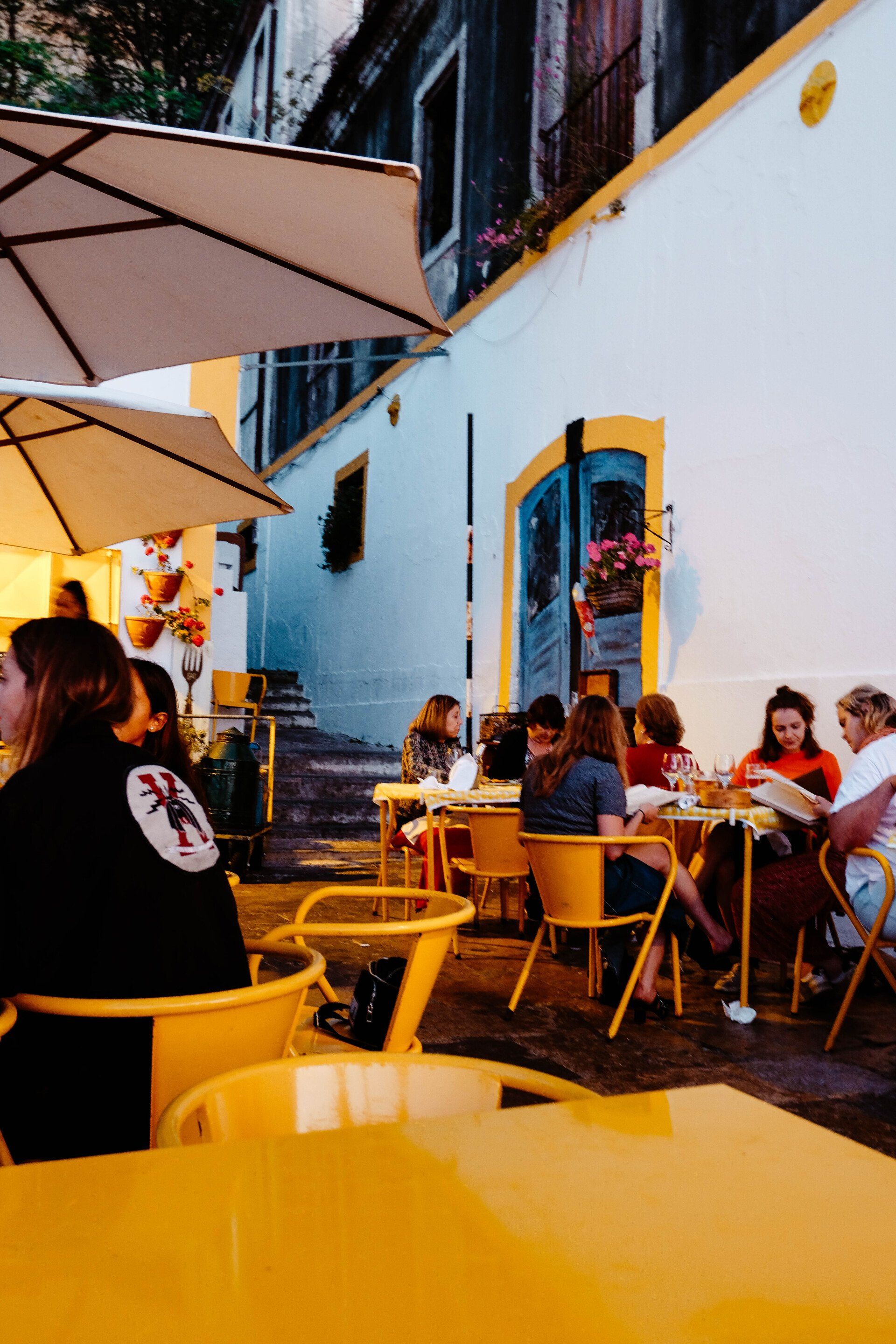 A group of people are sitting at yellow tables under umbrellas