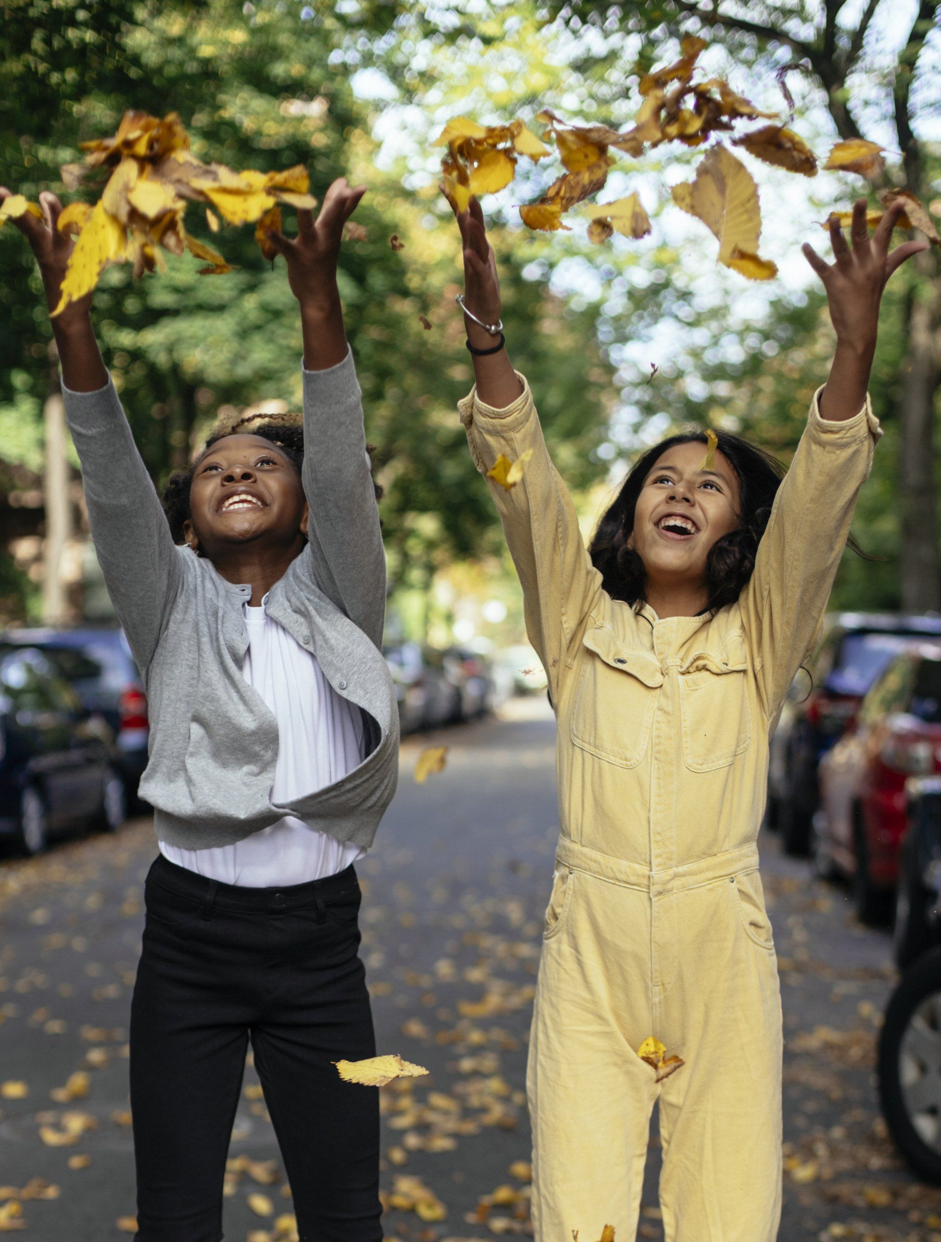Two people toss autumn leaves into the air on a city street.