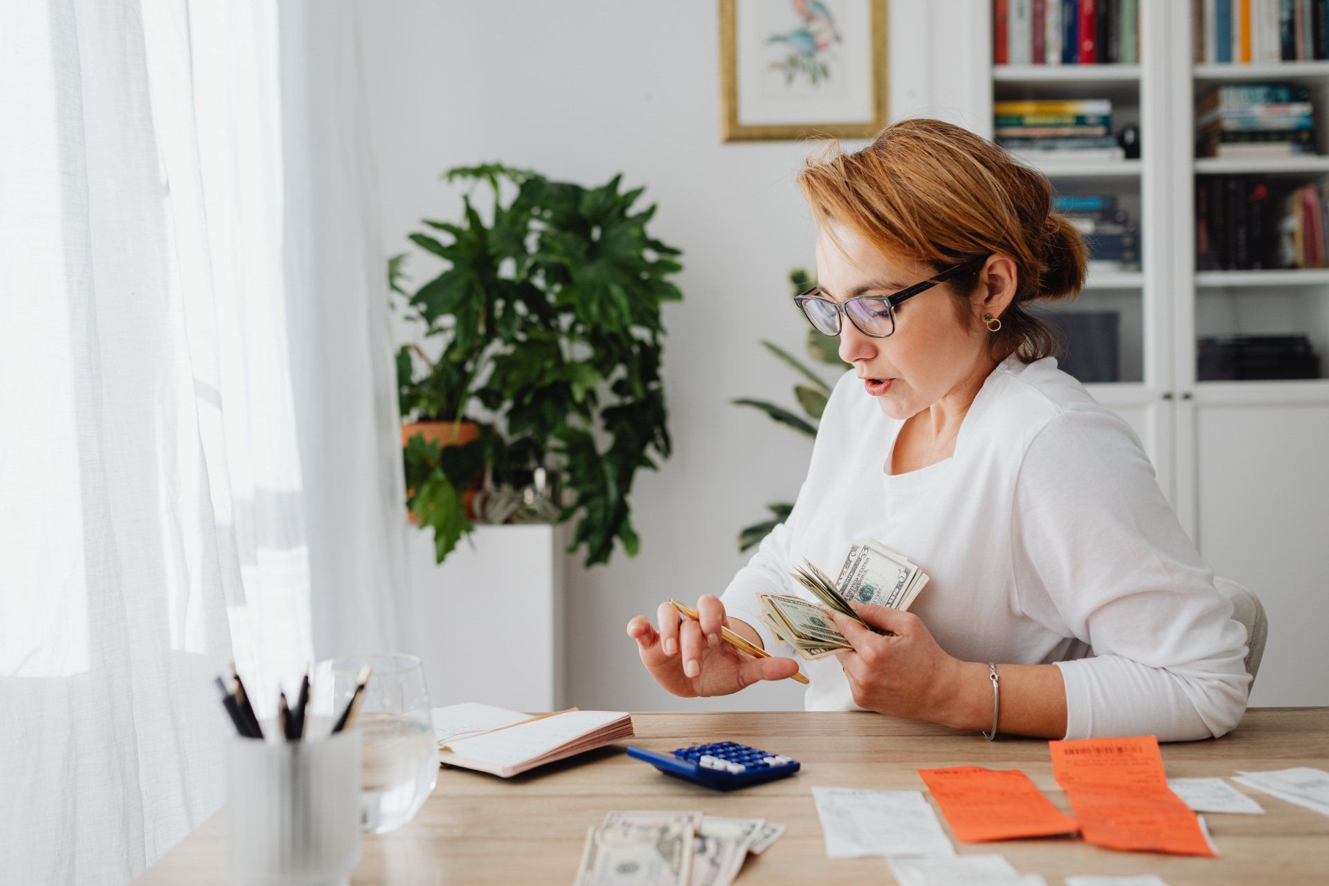 A woman at her desk counting money and creating a budget.