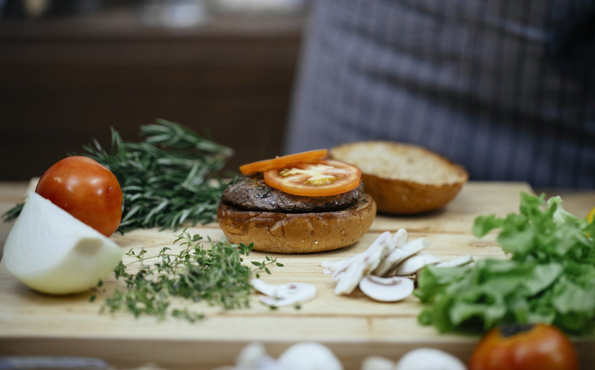 A hamburger is sitting on top of a wooden cutting board surrounded by vegetables.