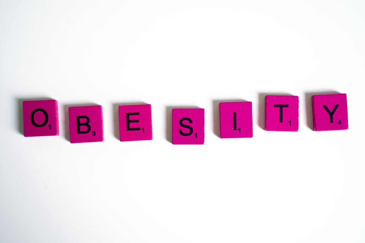 The word obesity is written on pink scrabble tiles.