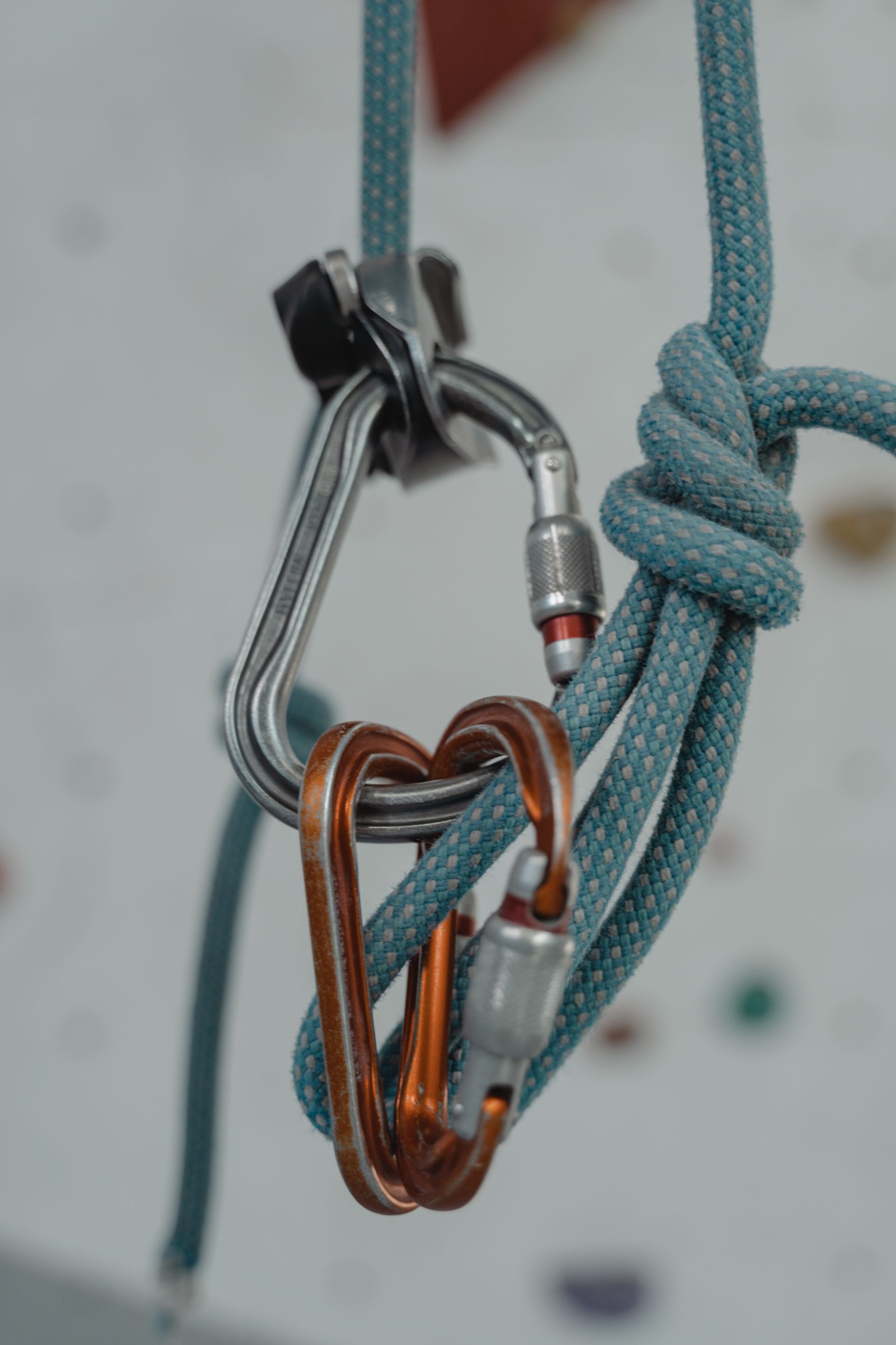 Climbing rope secured by two carabiners and a knot against a white climbing wall.