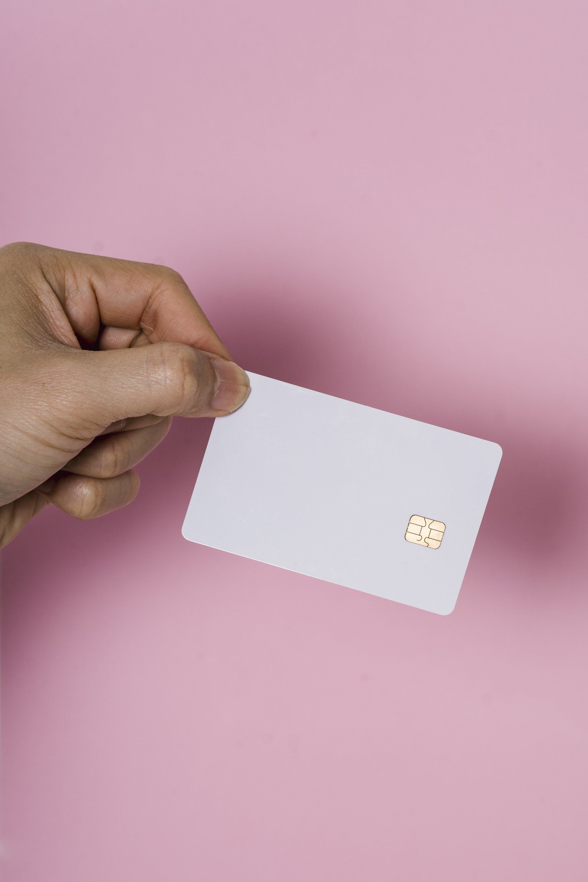 A person is holding a credit card in their hand on a pink background.