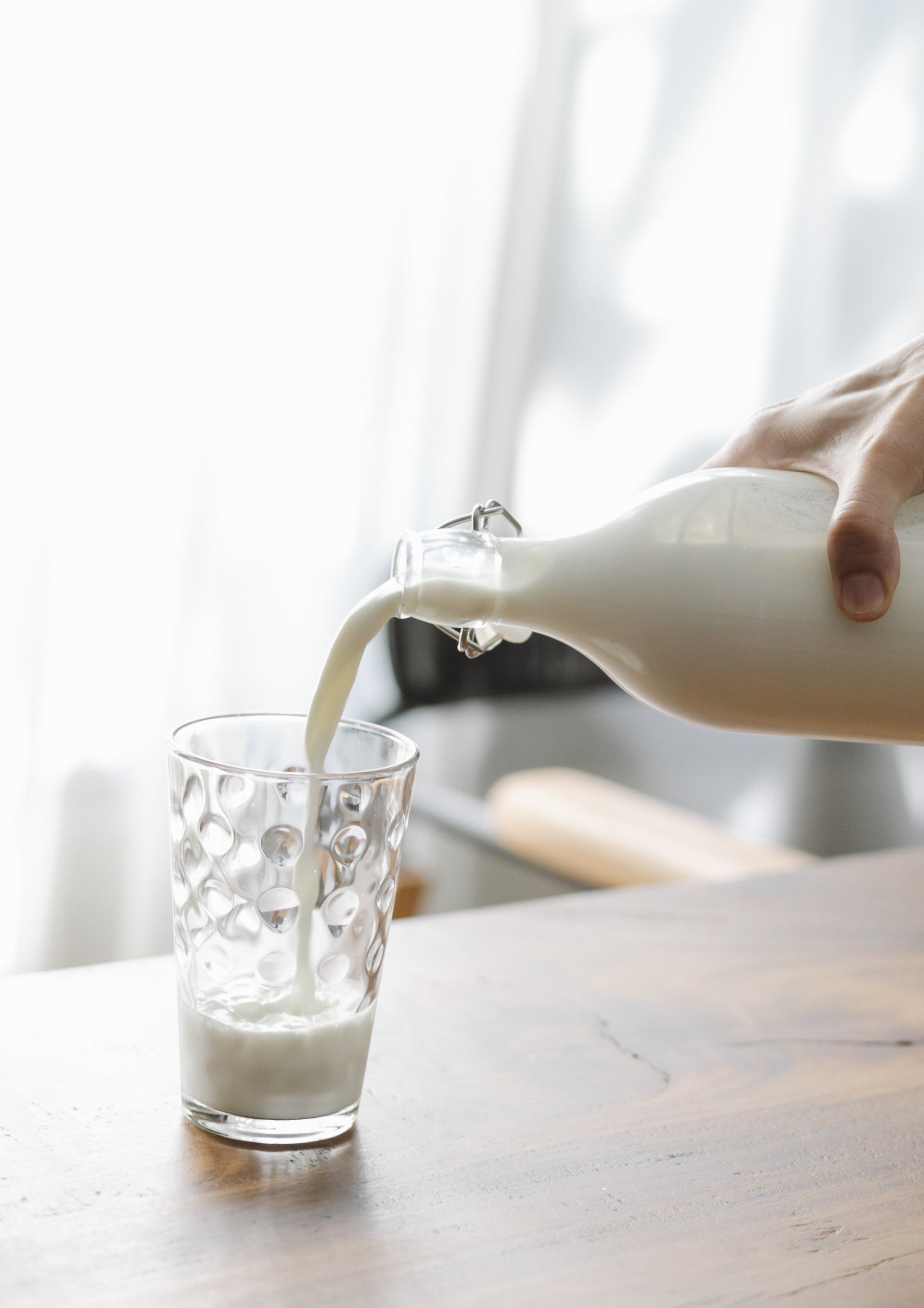 A person is pouring milk into a glass on a wooden table.