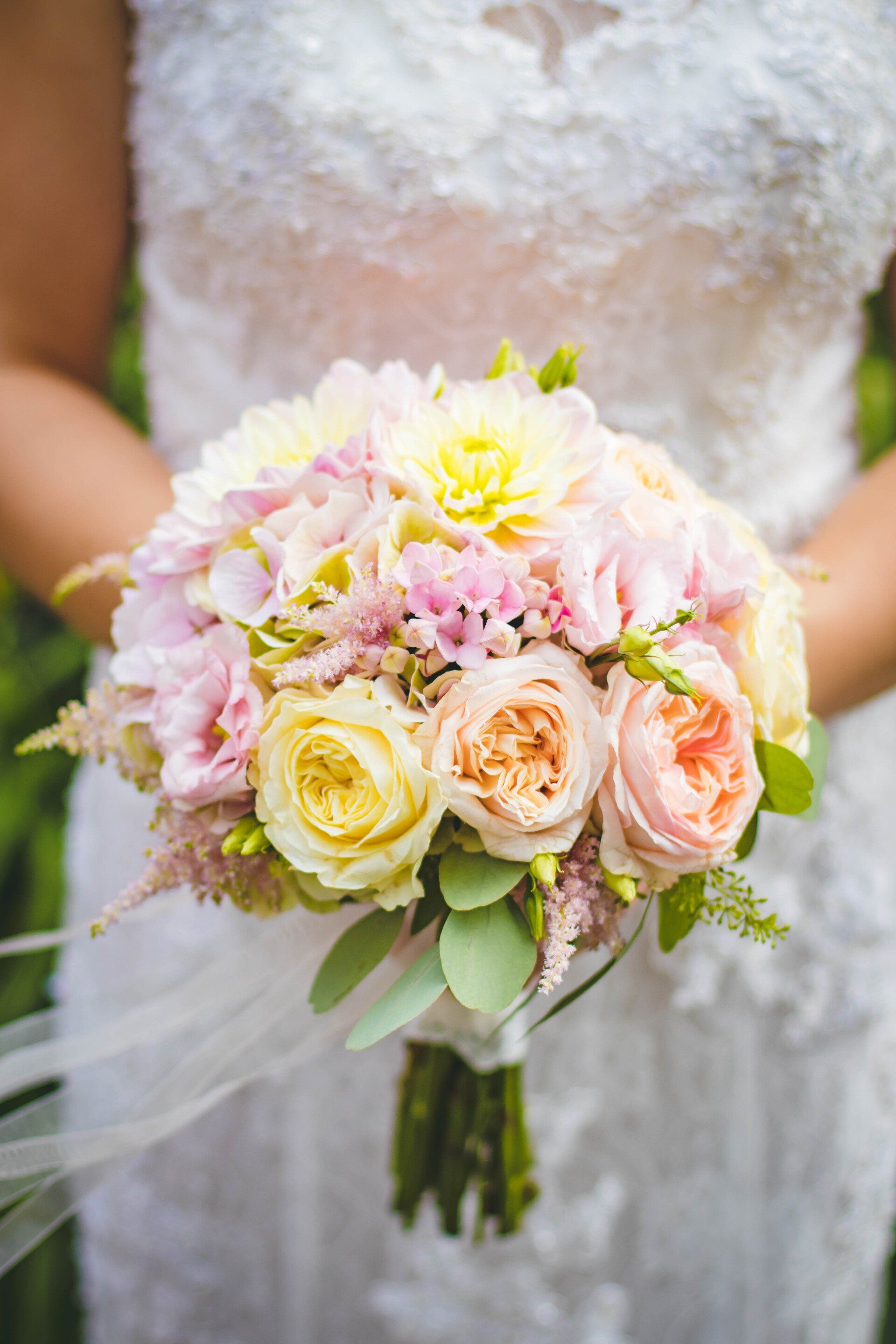 Een bruid in een witte jurk houdt een boeket van roze en gele bloemen vast