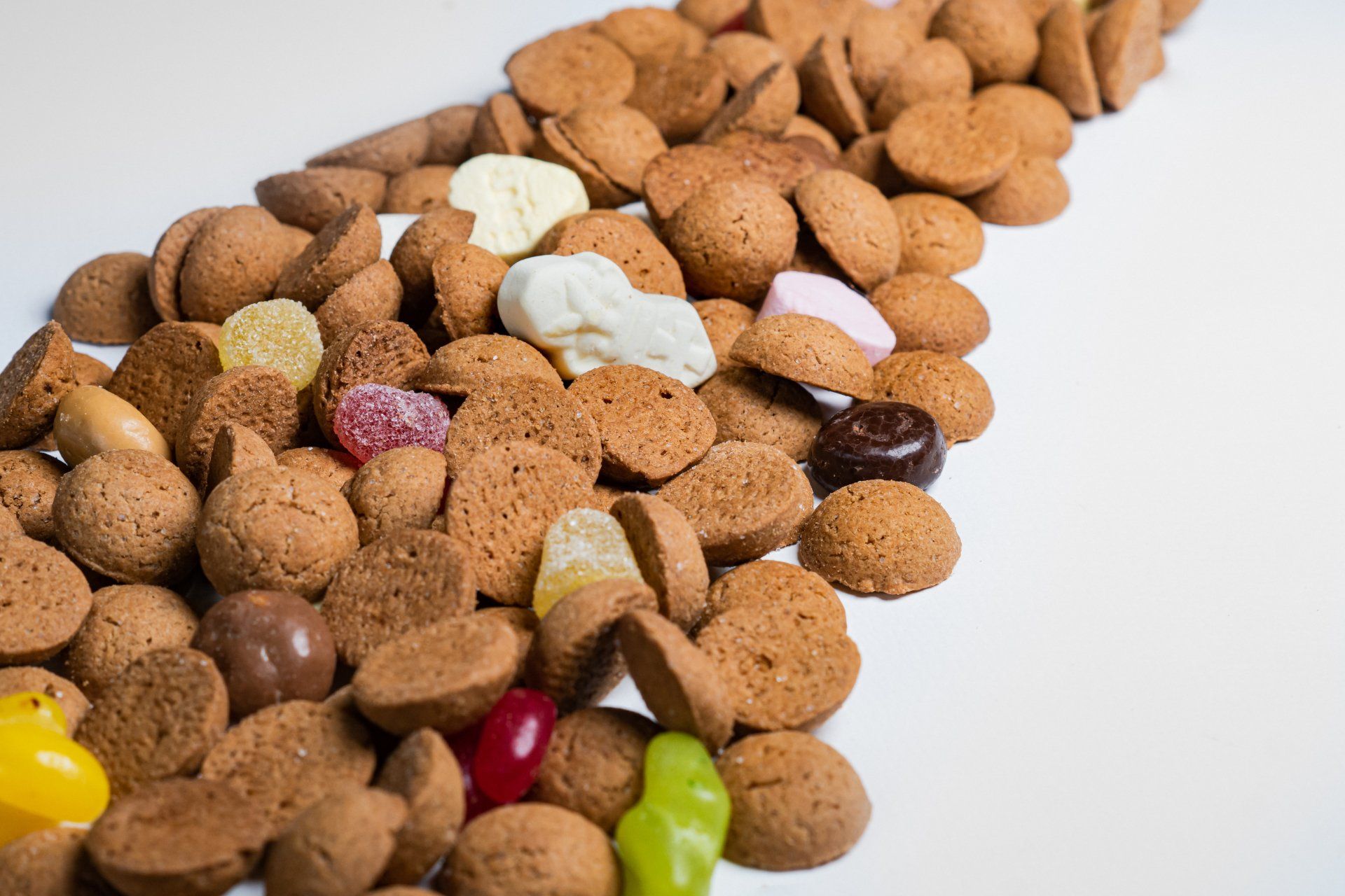 Een stapel Nederlandse pepernotenkoekjes en -snoepjes op een witte ondergrond.