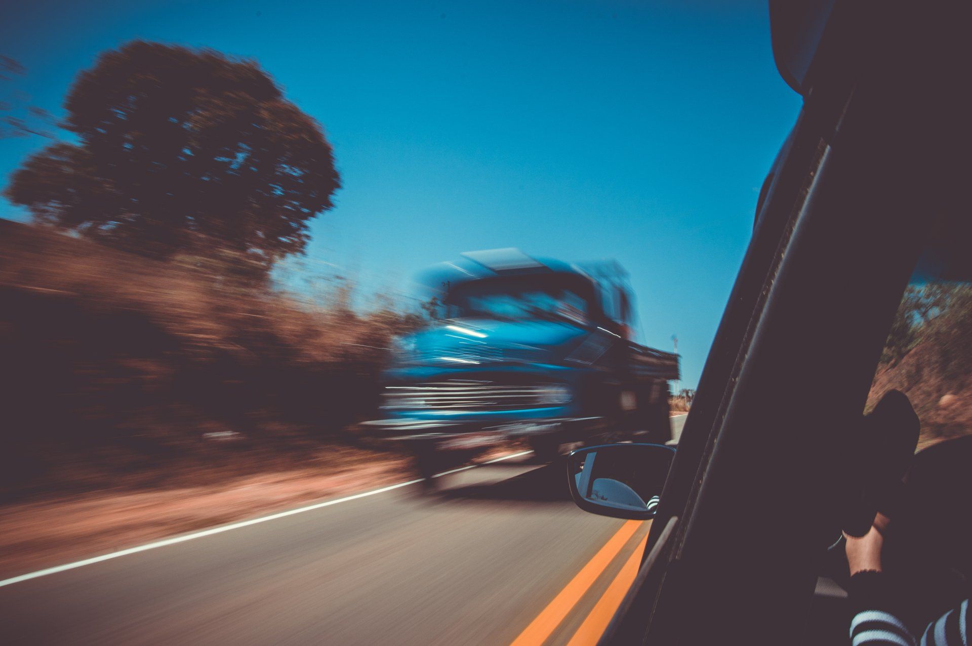 Blurred view from a moving car at night, with headlights streaking past trees and a truck ahead.