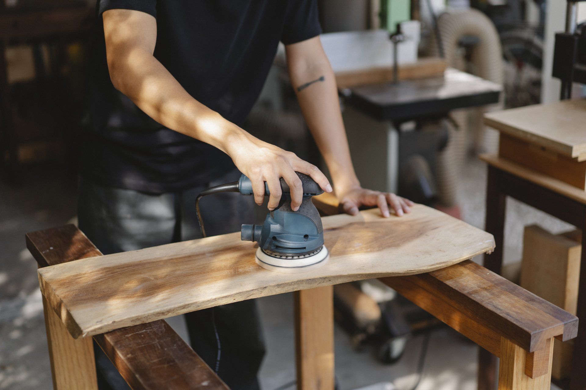 Person sanding a wooden board with a power sander in a workshop
