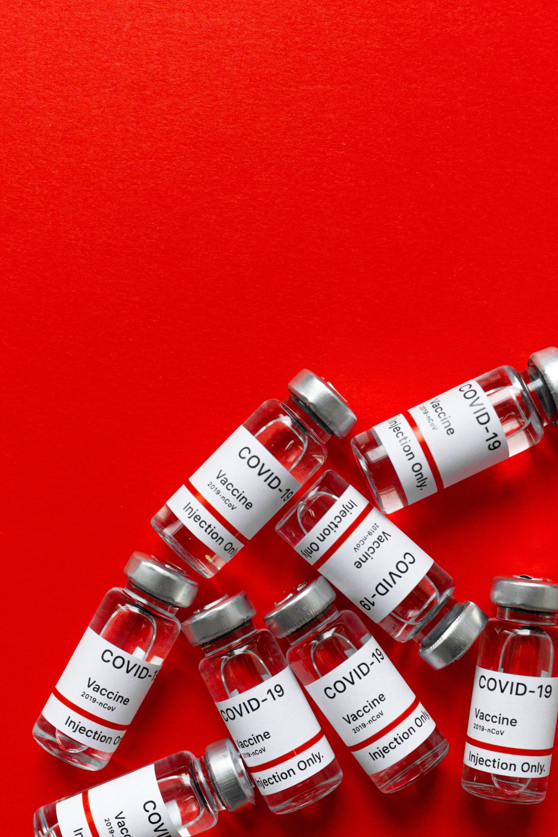 A bunch of bottles of covid-19 vaccine on a red background.
