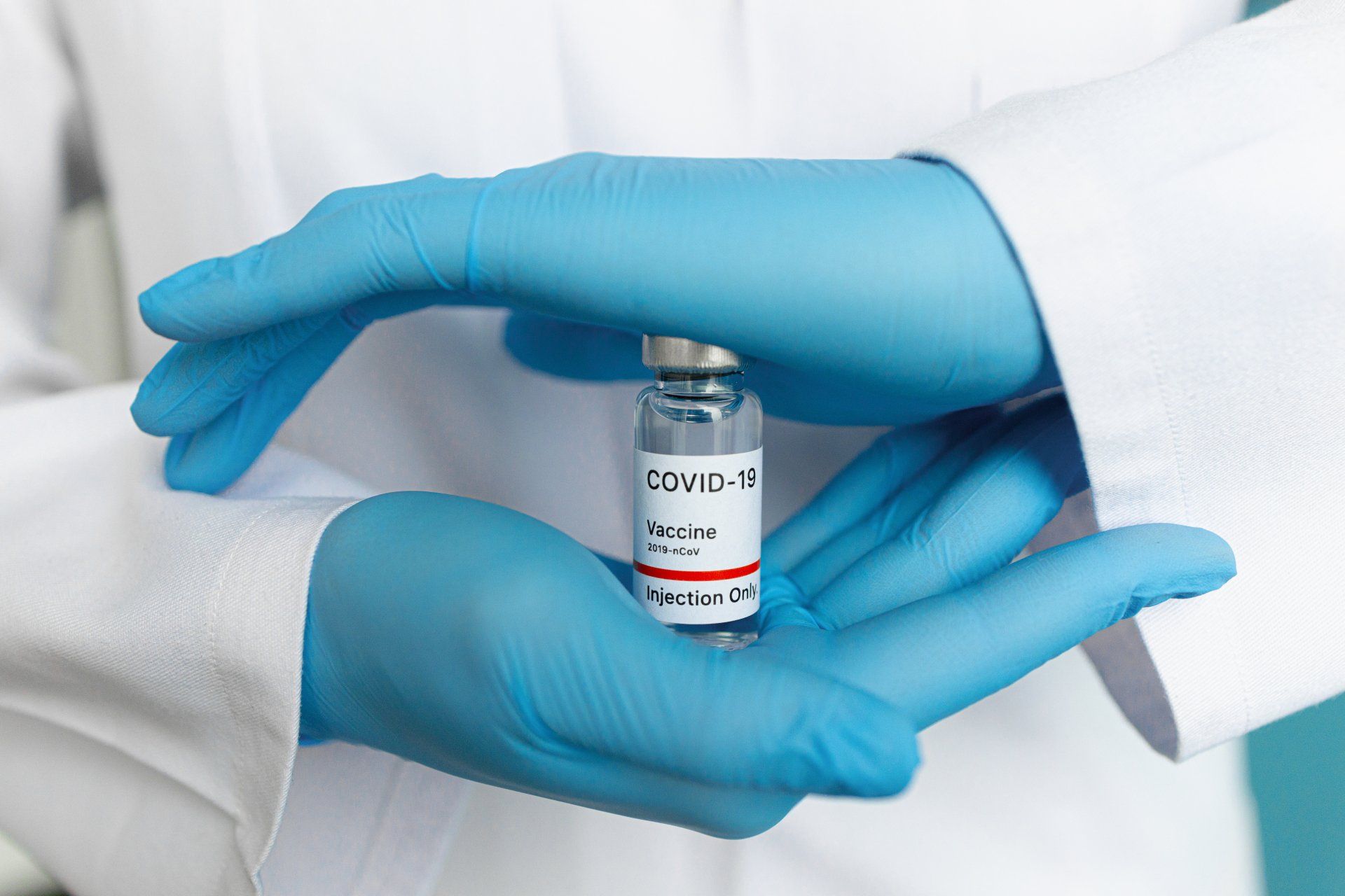 A person wearing blue gloves is holding a bottle of covid-19 vaccine.