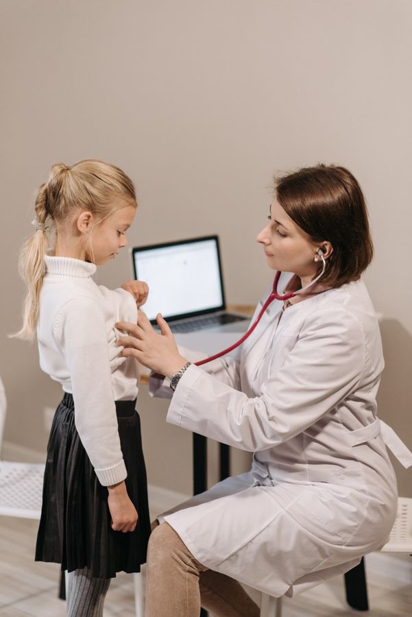 A doctor is listening to a little girl 's chest with a stethoscope.