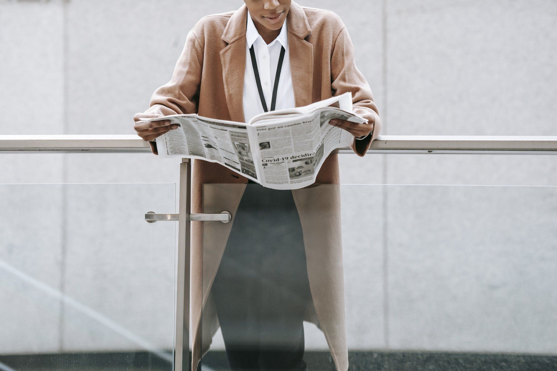 A man is standing next to a railing reading a newspaper.