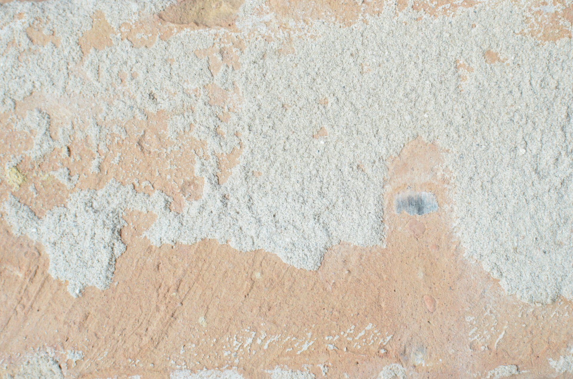 Peeling beige wall paint with white patches and a rough, weathered texture