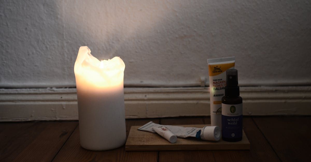 A lit white candle next to skincare products on a wooden surface.