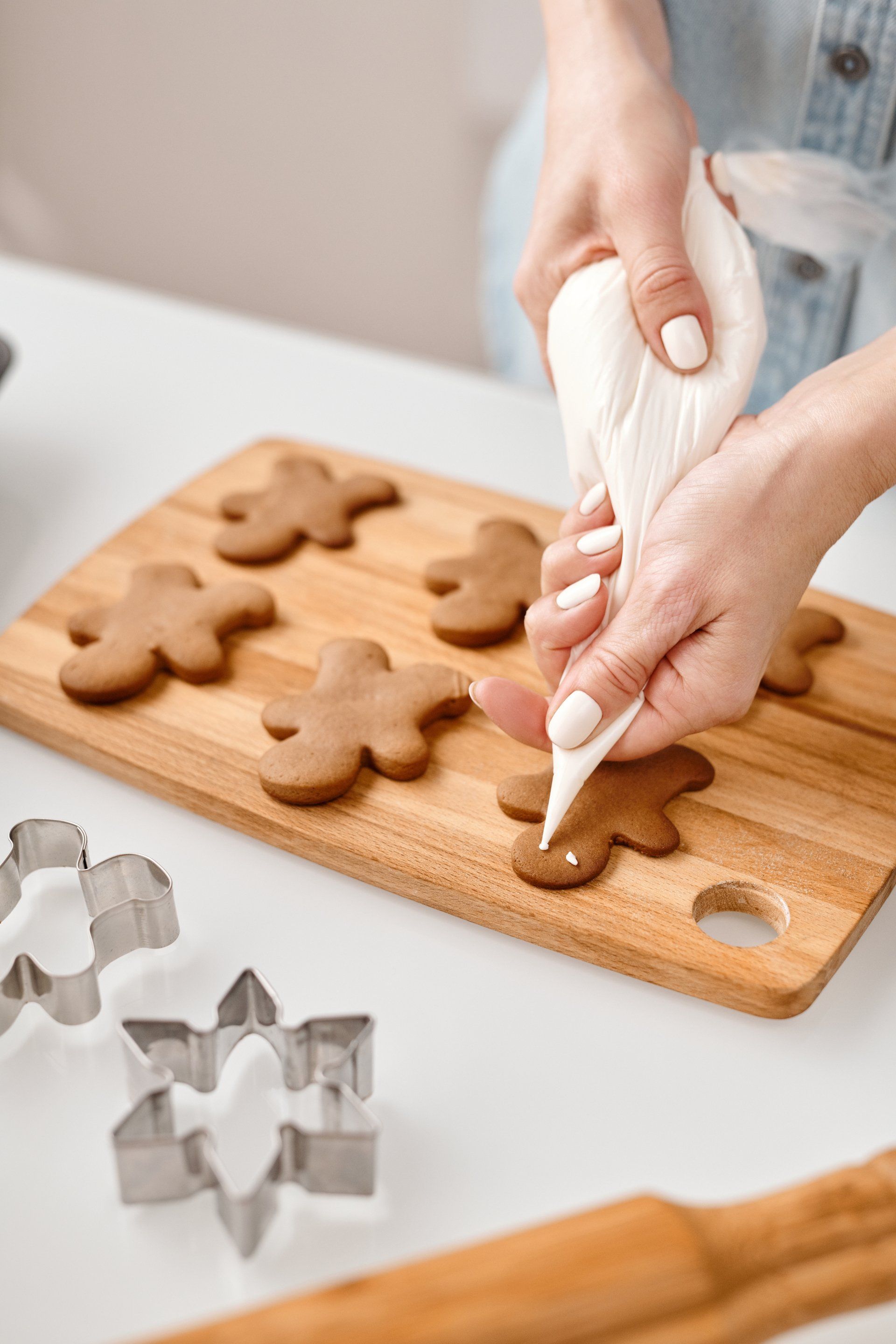A person decorating gingerbread men cookies on a wooden board with a white icing piping bag.