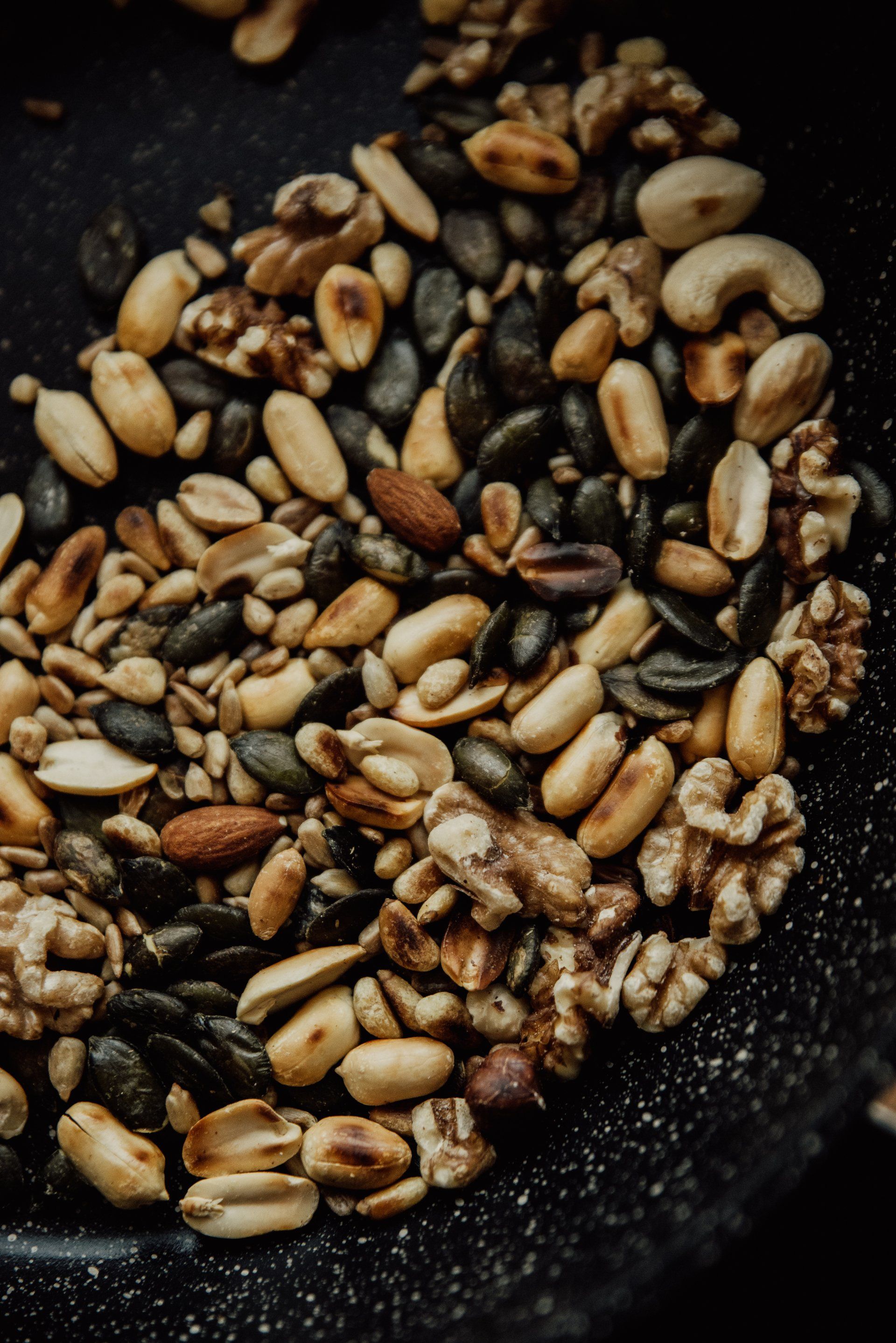 Toasted mixed nuts in a black pan, close-up