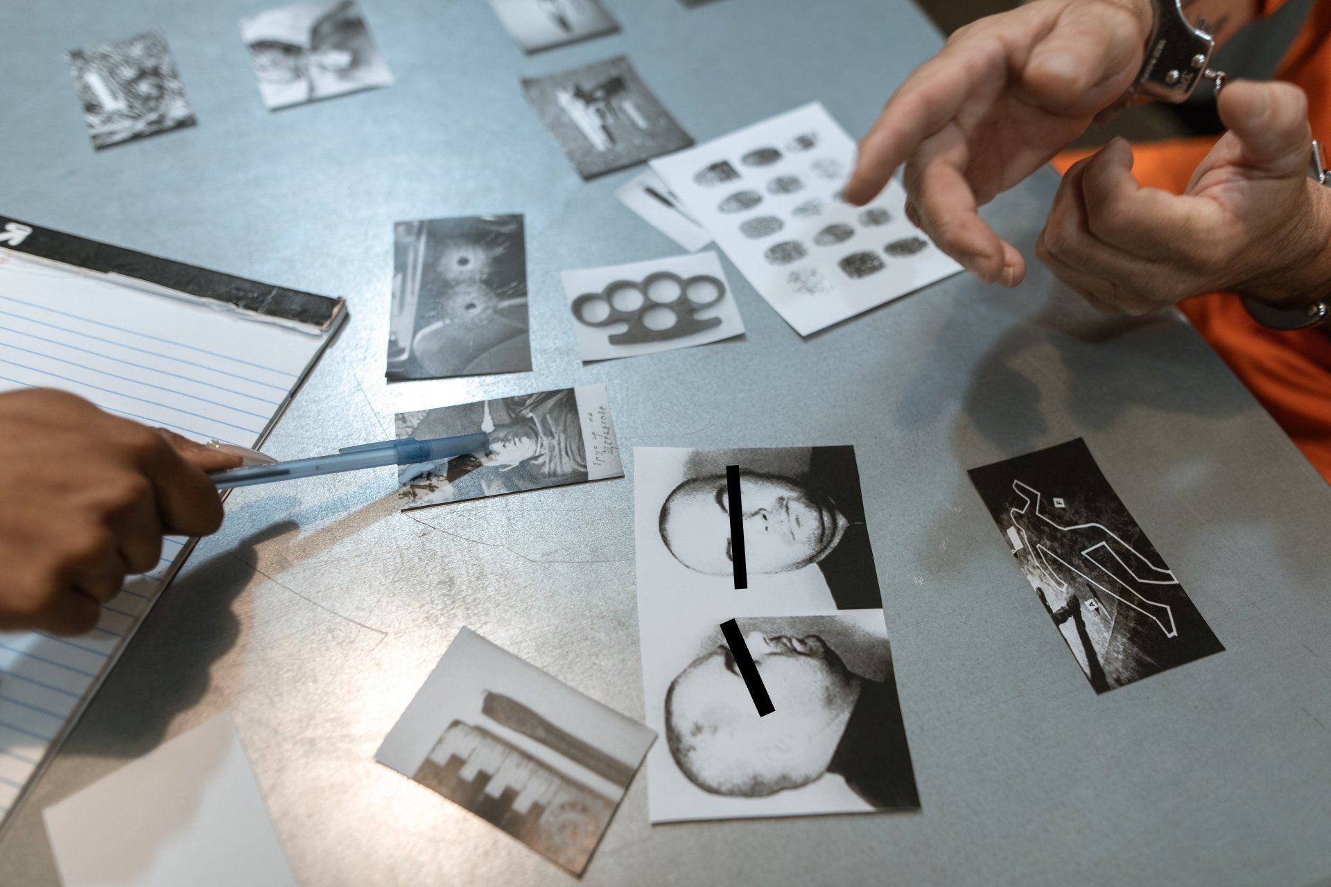 Hands reviewing black-and-white photo prints on a tabletop with notes and scissors