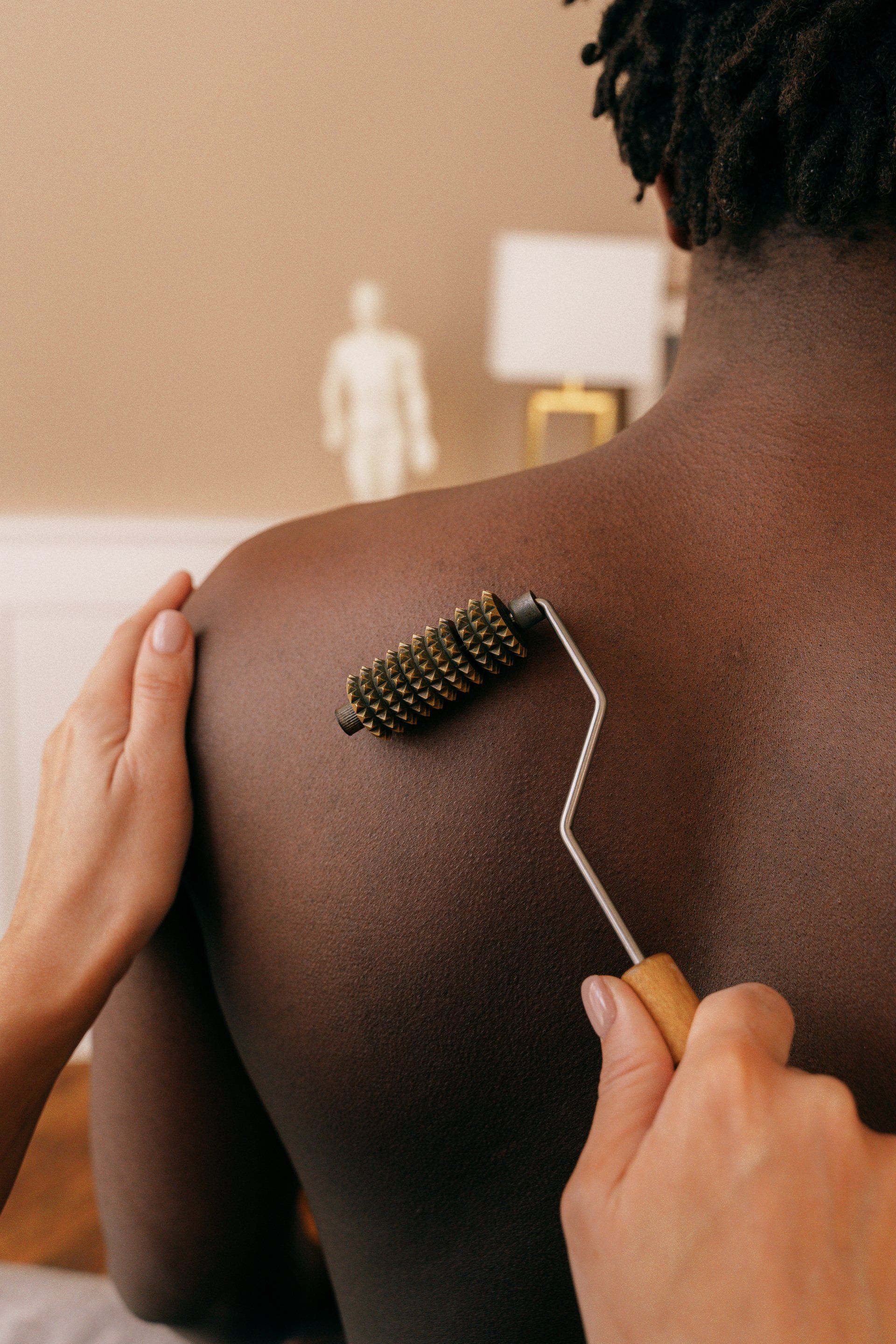 A person is using a roller on a man 's back.