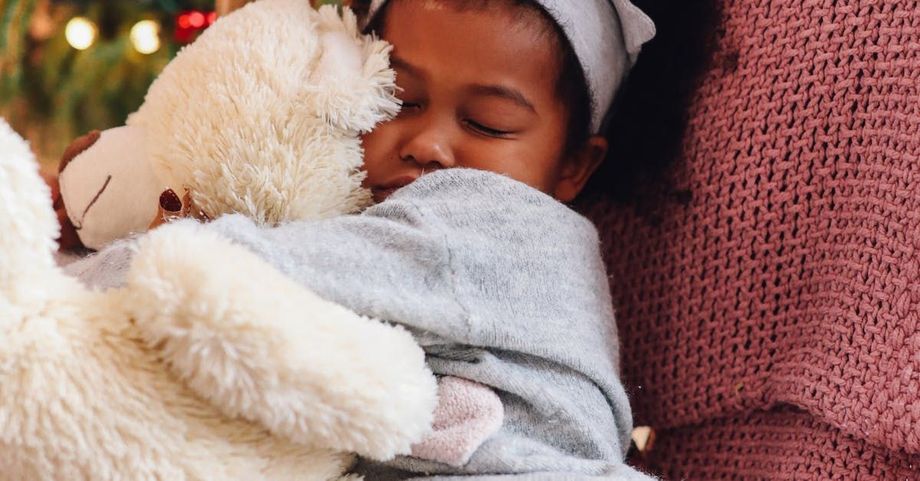 A little girl is hugging a teddy bear in front of a christmas tree.