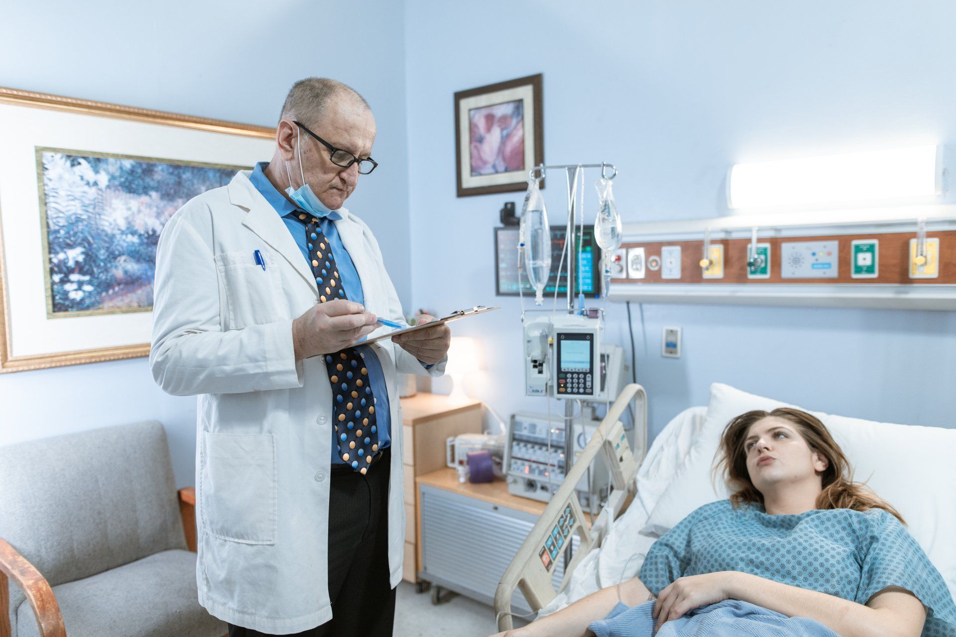 A woman is talking to a woman with cancer in a hospital chair.