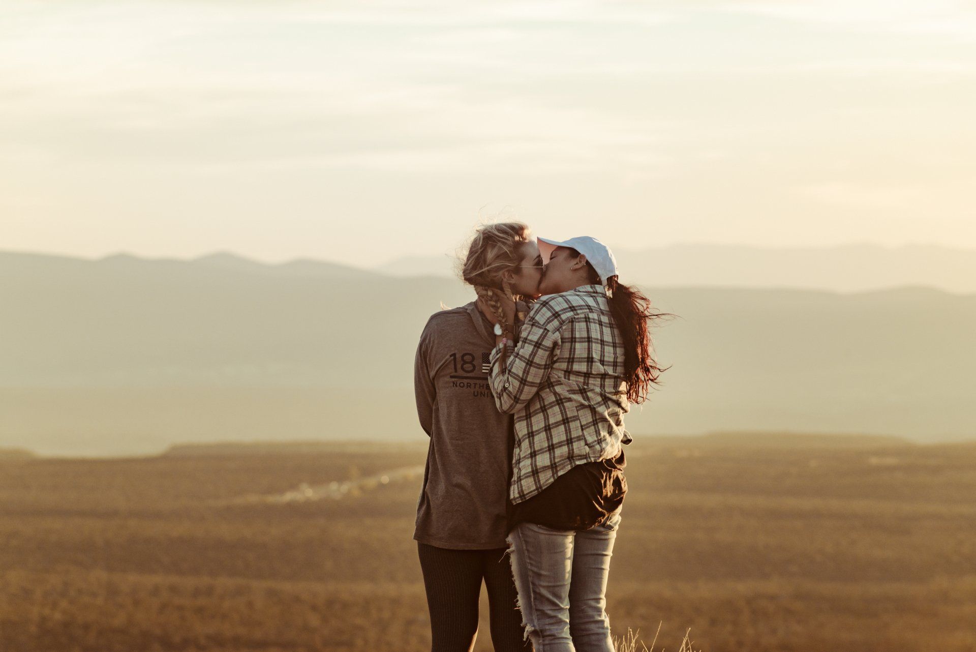 Two women kissing outside in front of mountains