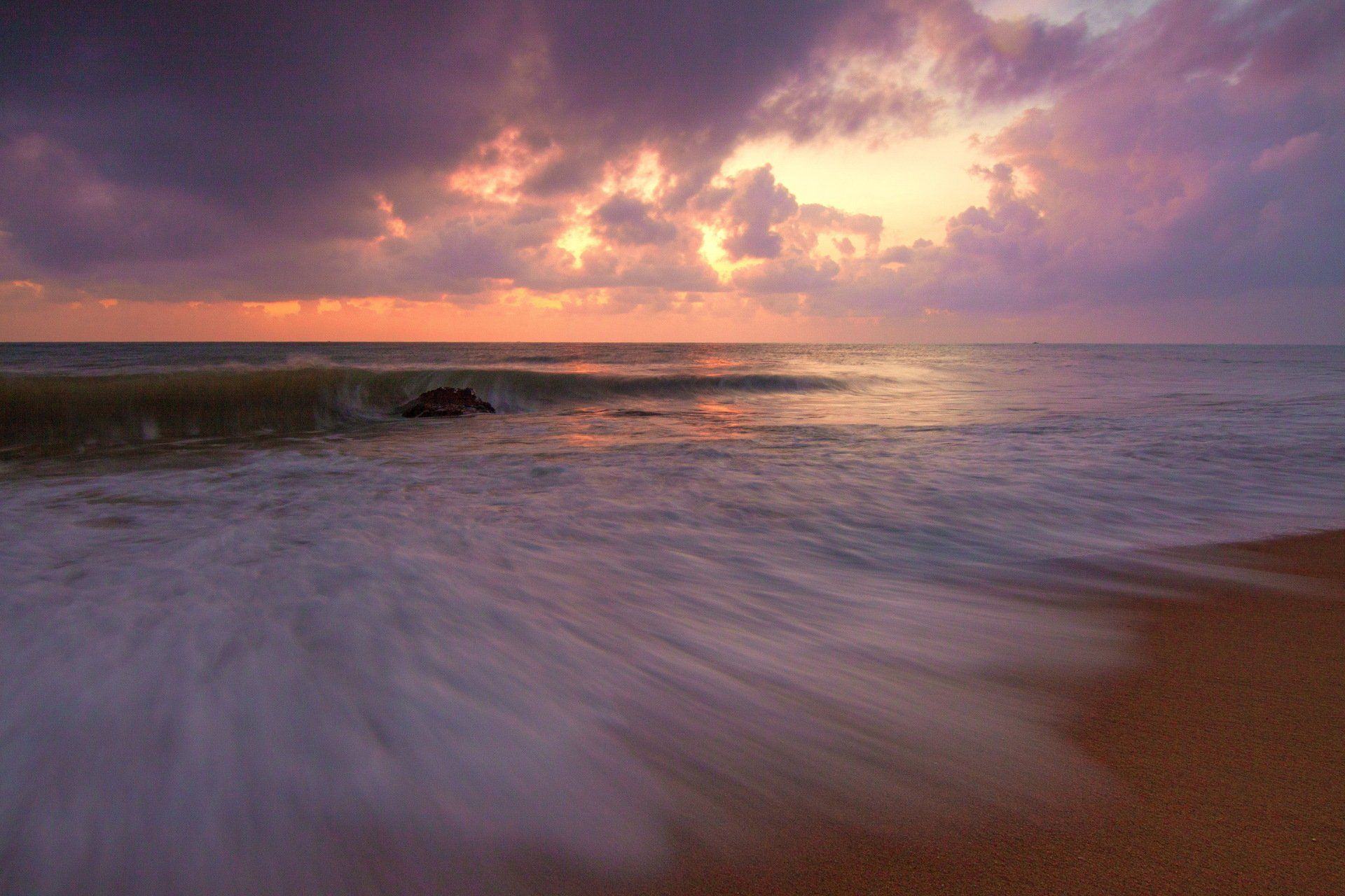 The sun is setting over the ocean and the waves are crashing on the beach.