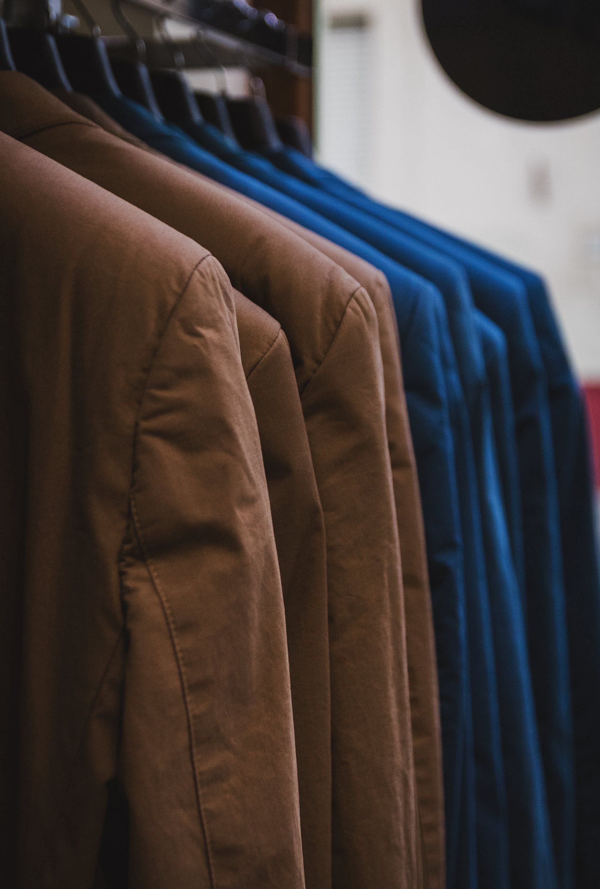 A row of suit jackets hanging on a rack, with brown jackets in the foreground and blue jackets in the background.