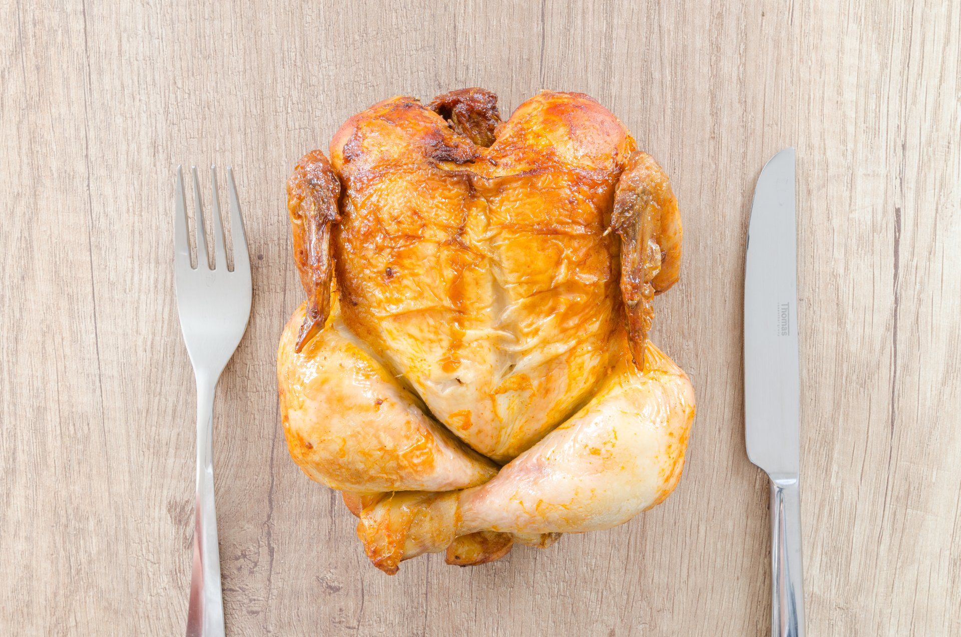 A propane grilled chicken on a table with a knife and fork.