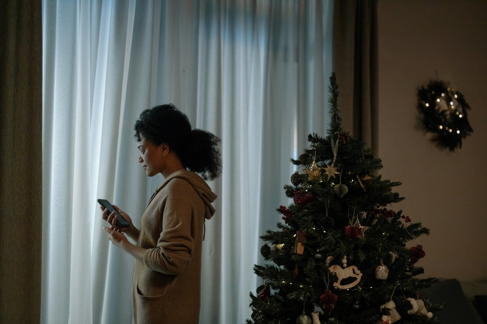 A woman is standing in front of a christmas tree looking at her phone.