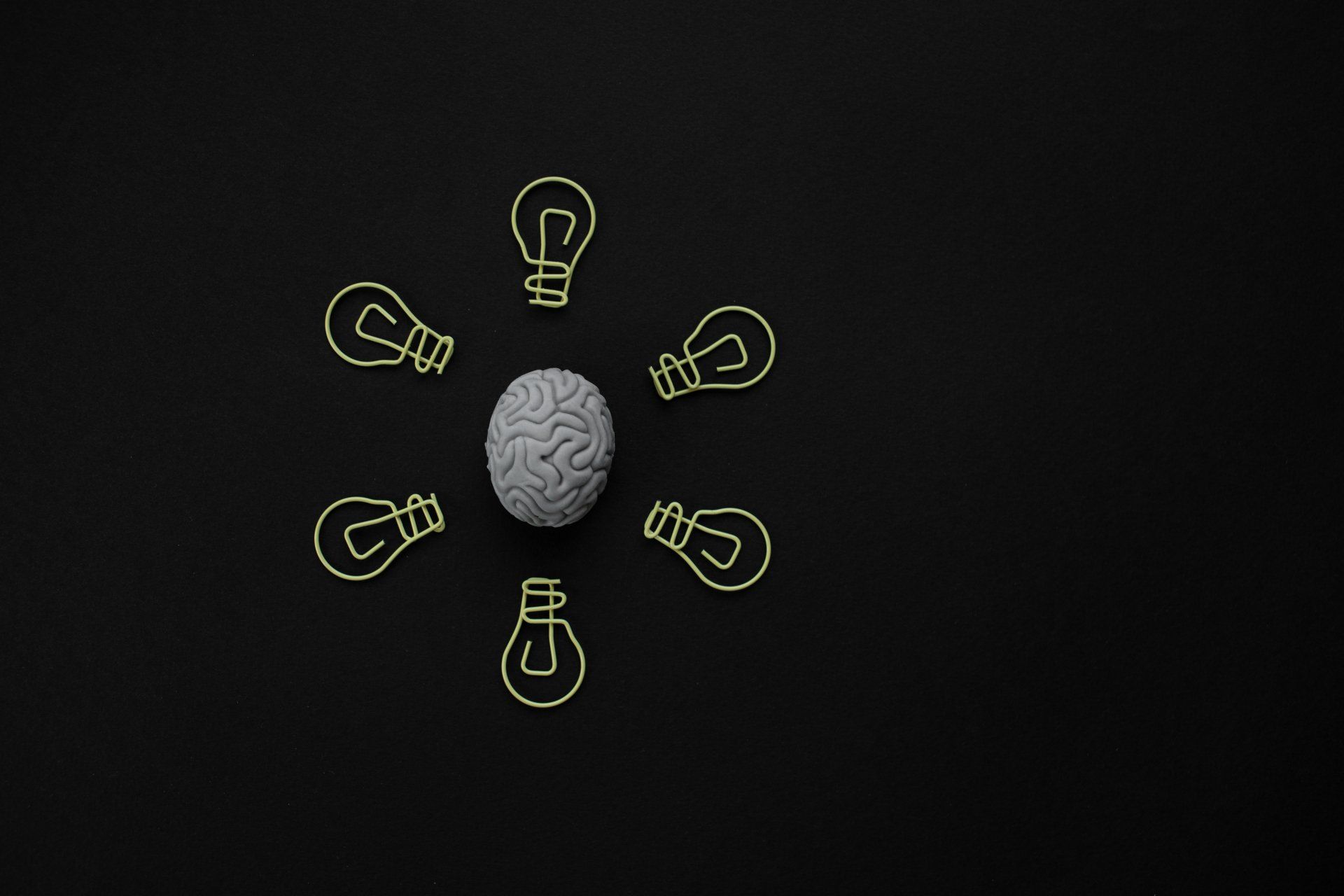 A brain is surrounded by light bulbs on a black background.
